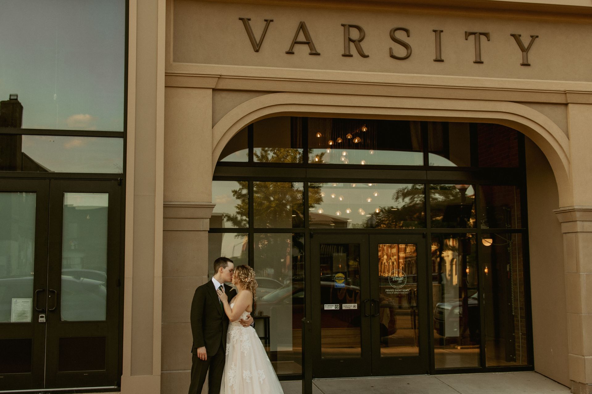 Bride and groom kissing outside a building labeled “VARSITY”
