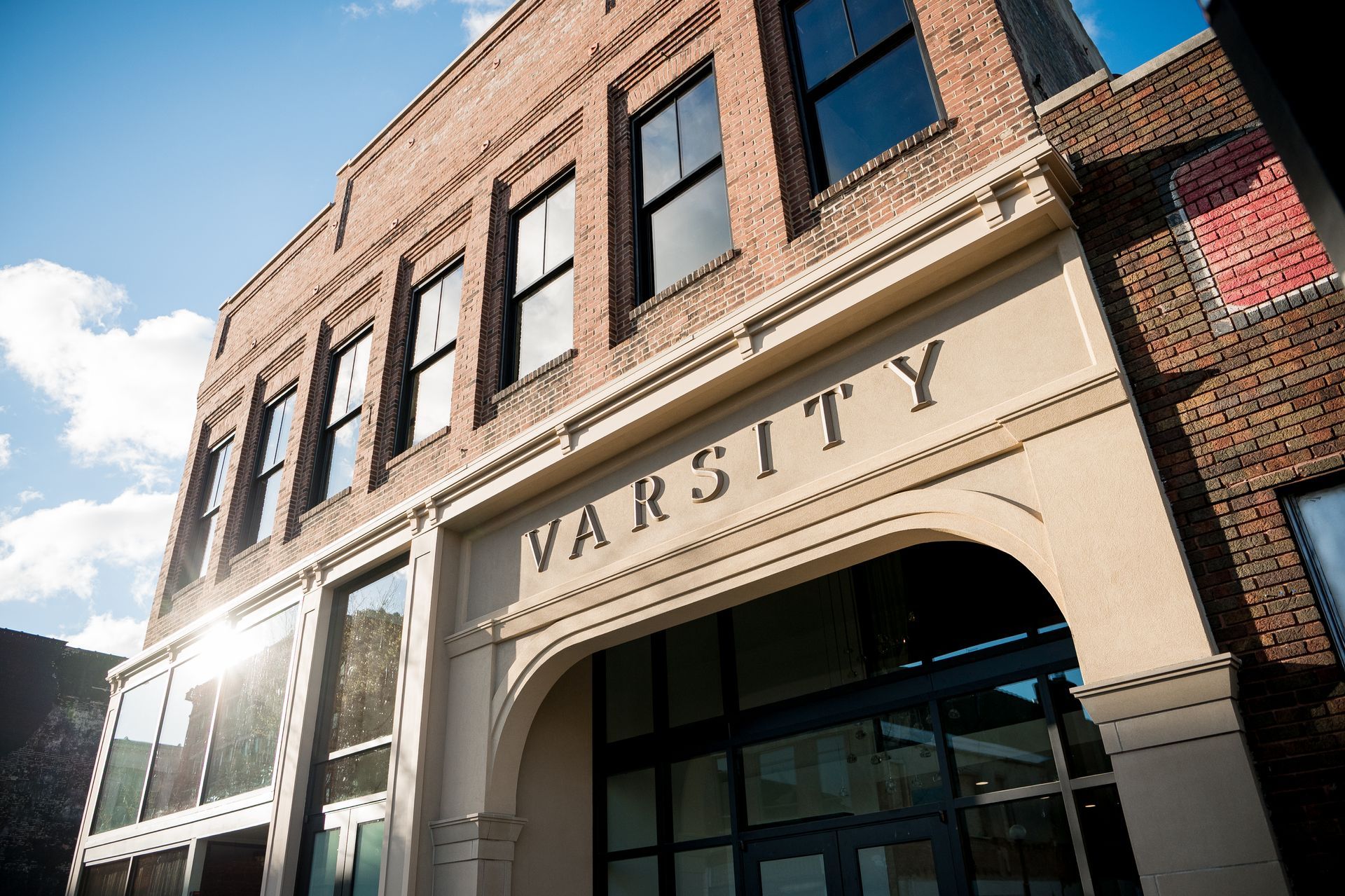 Brick university building entrance with large “VARSITY” sign under a blue sky