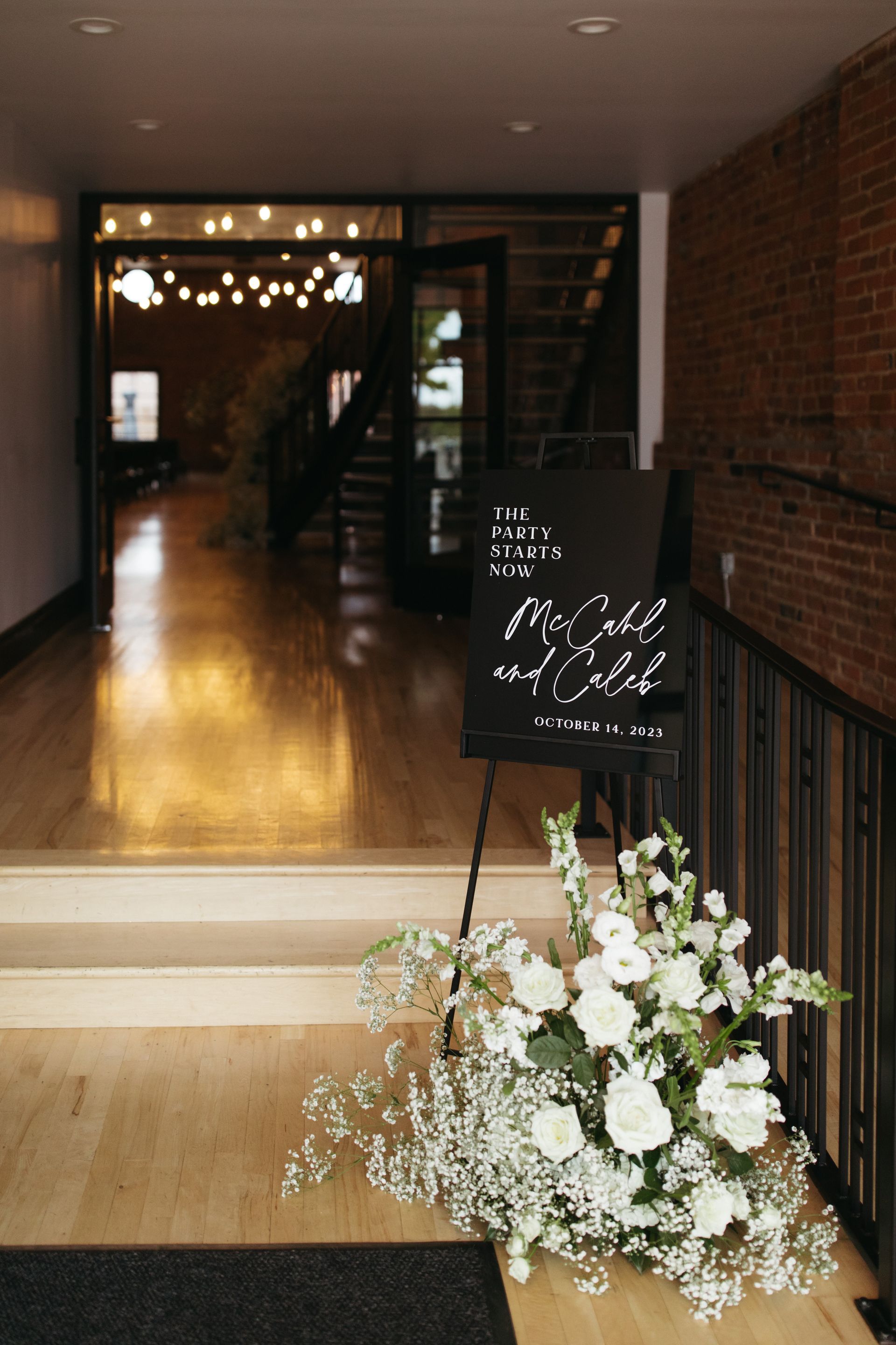 Wedding welcome sign beside white floral arrangement at an indoor venue entrance