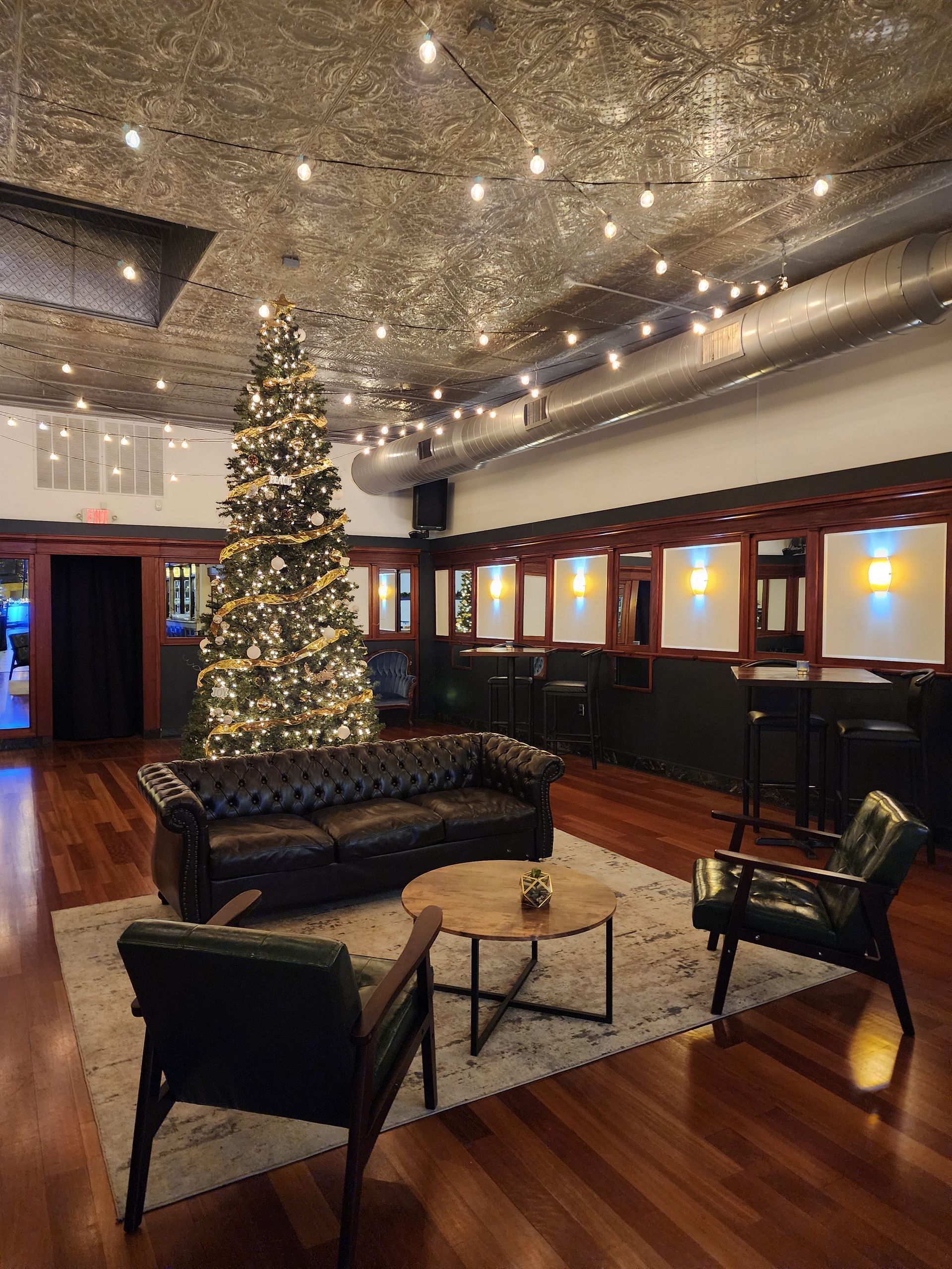 Festive lounge with Christmas tree, dark leather seating, and warm string lights on a wooden floor