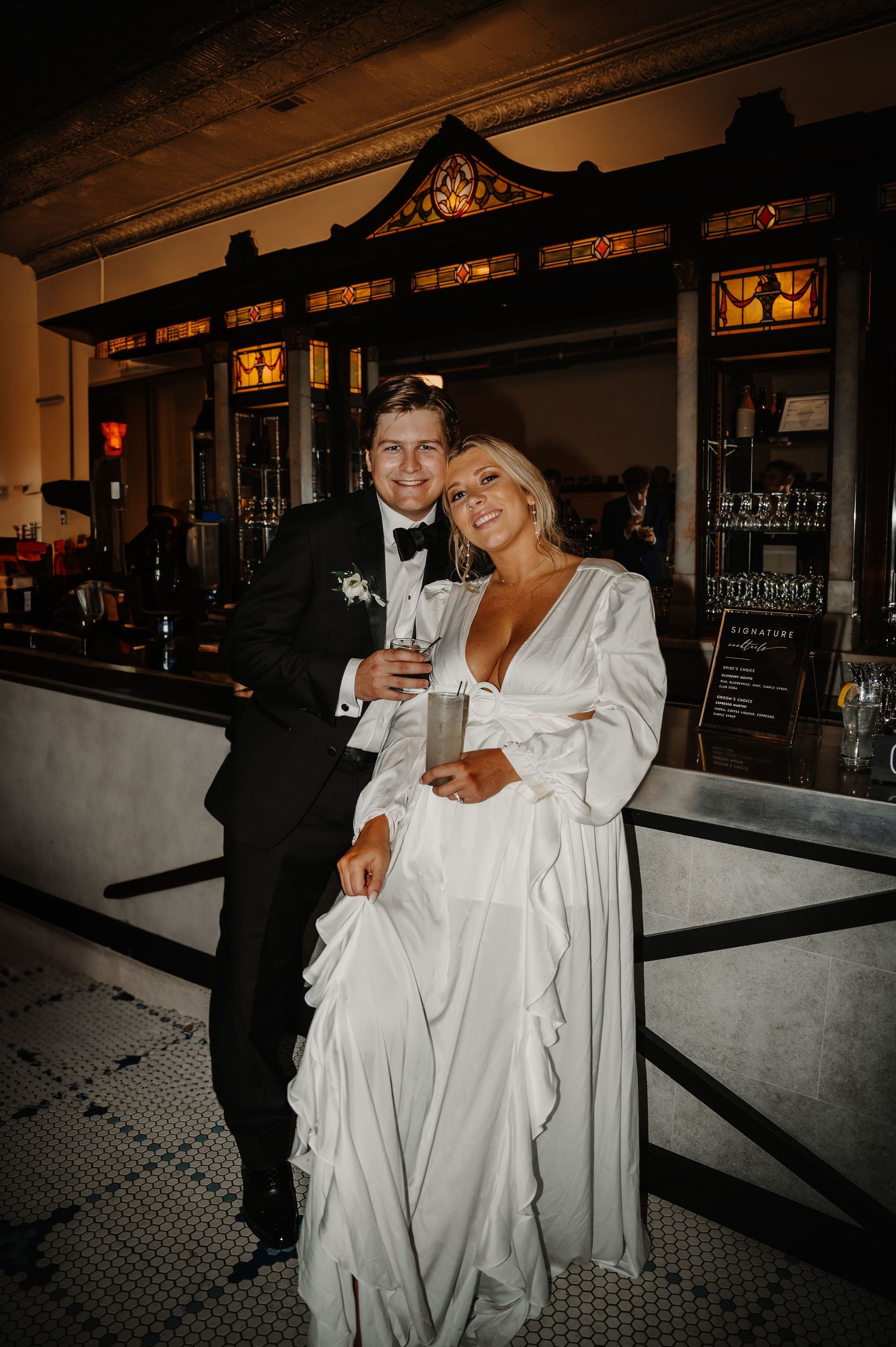 Couple posing in formal attire at night outside an ornate building, holding drinks and smiling