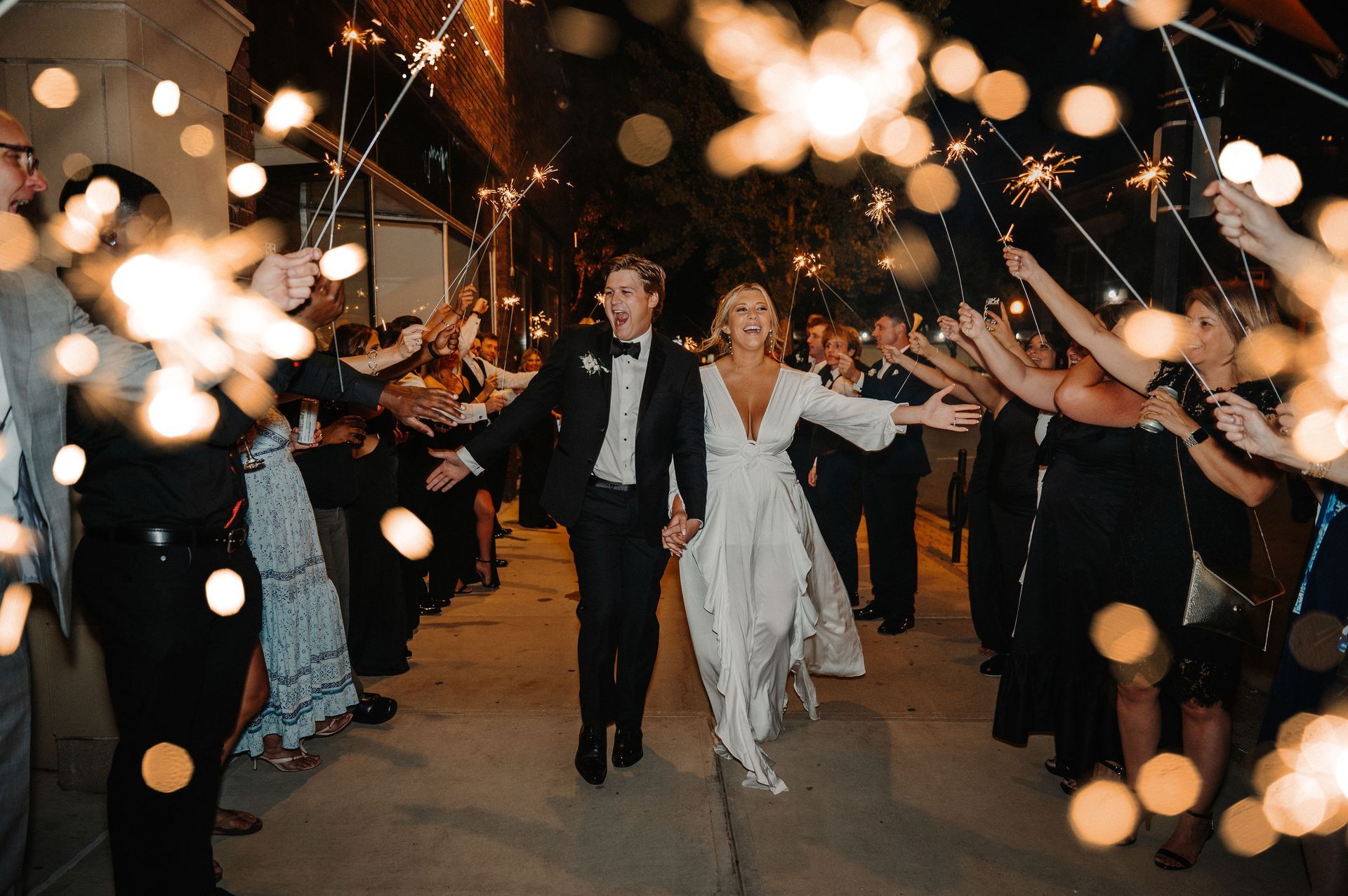 Newlyweds walking through a sparkler send-off tunnel at a nighttime celebration