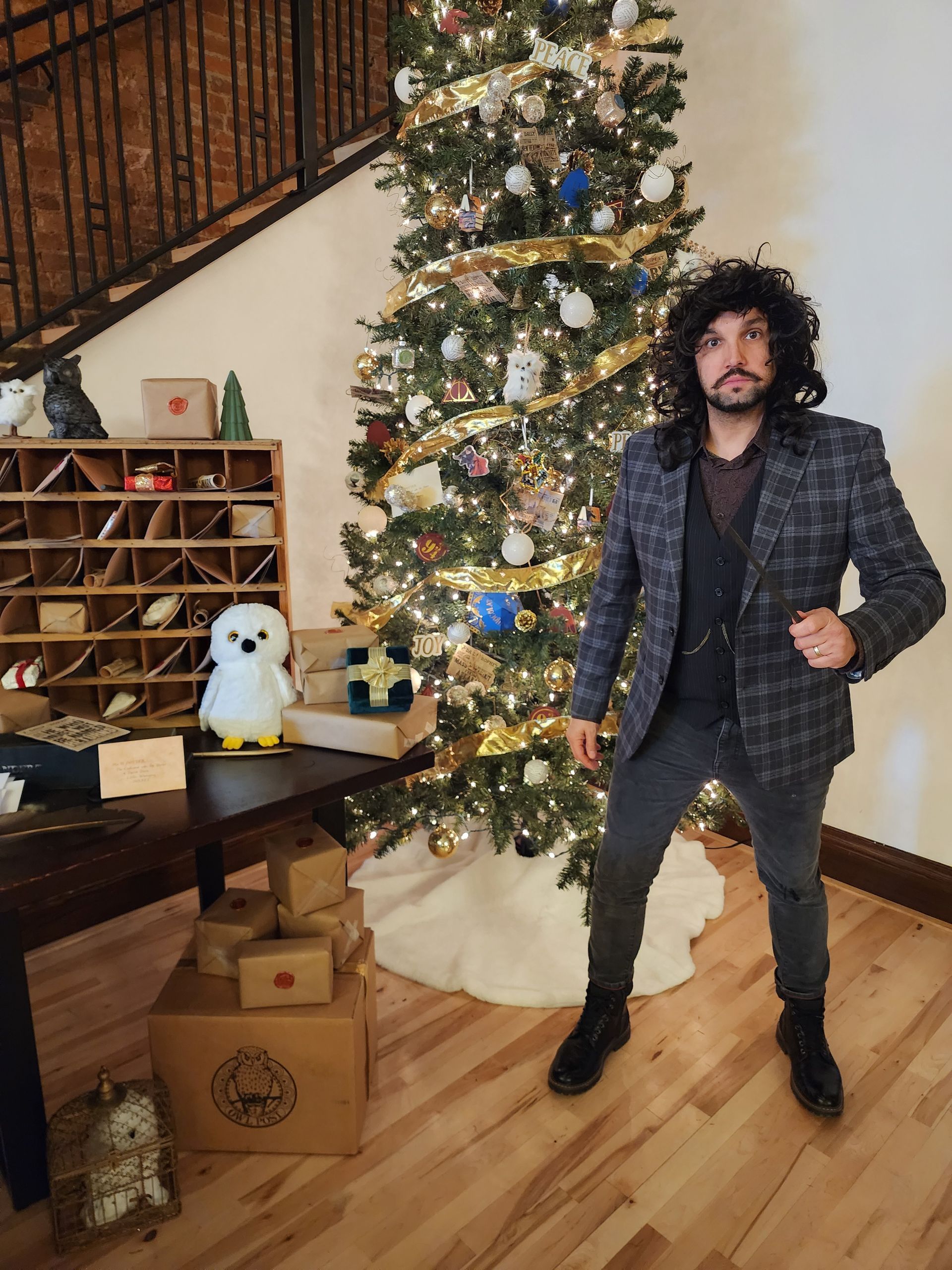 Man standing beside a decorated Christmas tree in a living room with wood floors and holiday decor