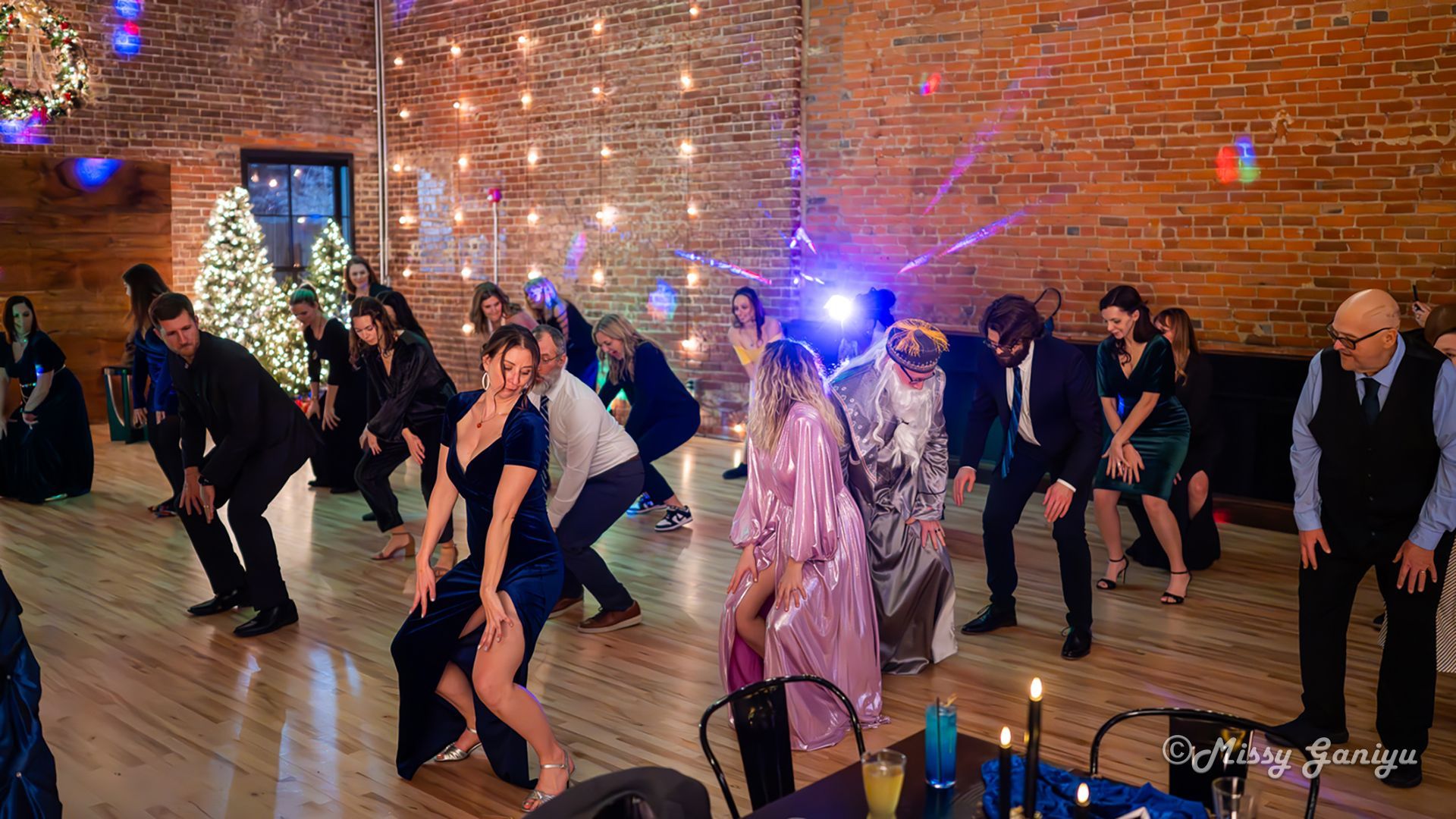 People dancing in a brick-walled hall at a formal party, with blue lights and one person in a pink dress.