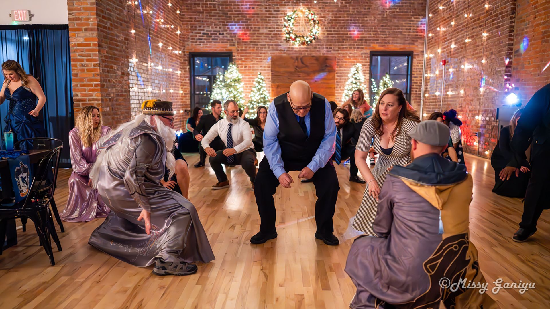 People dancing at a festive indoor event with string lights, brick walls, and wood flooring