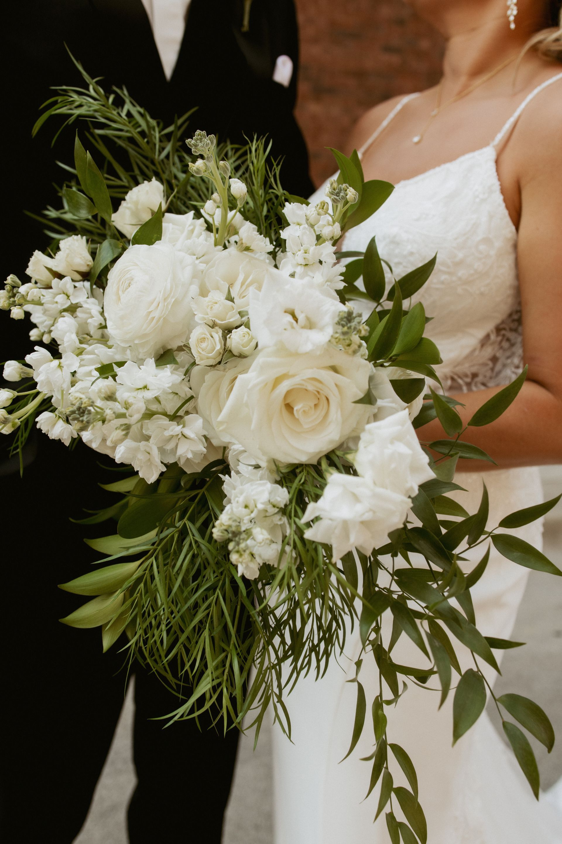 Bride holding white rose and greenery bouquet in a white lace wedding dress