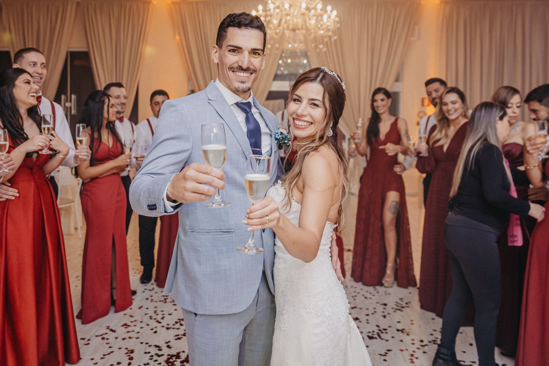 Bride and groom toasting with champagne at a wedding reception, surrounded by guests in formal attire