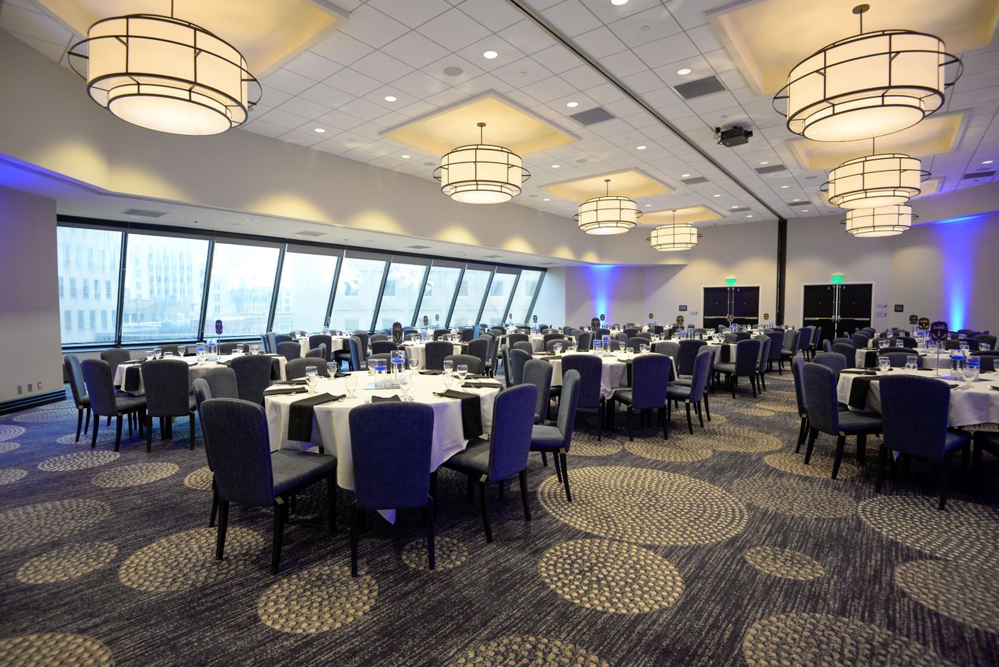 Elegant banquet hall with round tables, purple chairs, chandeliers, and large windows overlooking the water