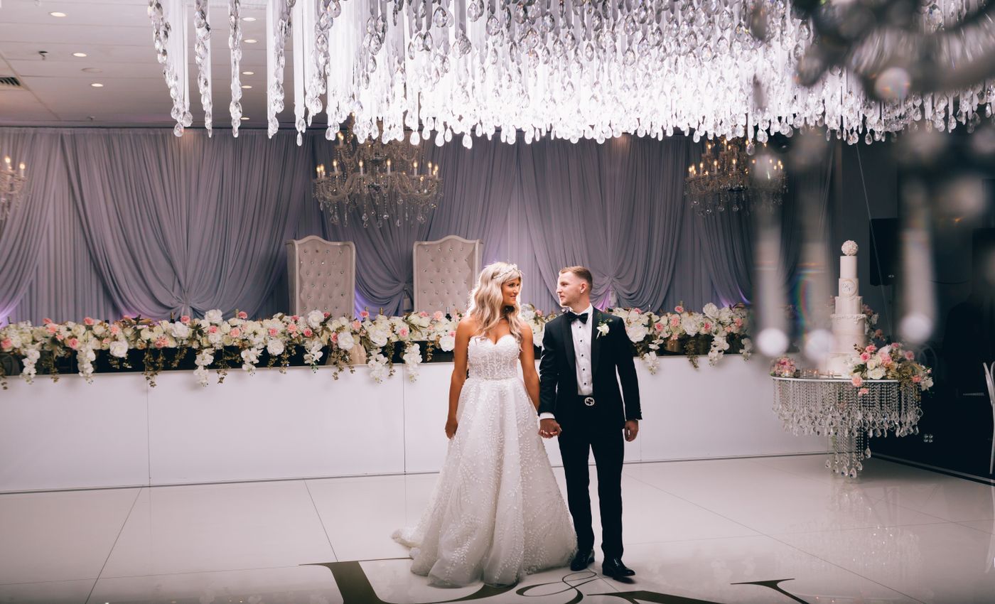 Bride and groom stand together on a decorated wedding stage under hanging lights.