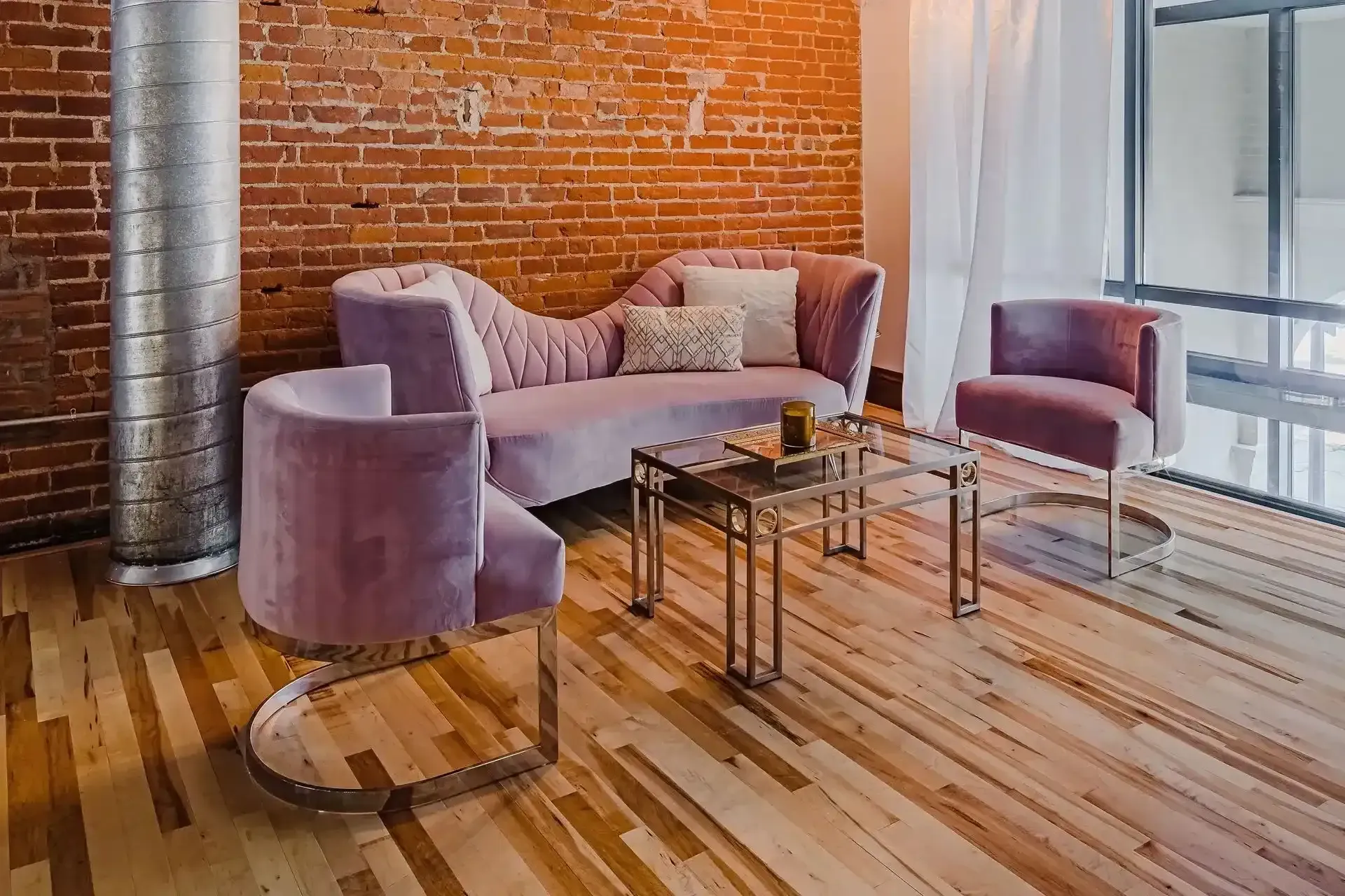 Modern lounge with purple chairs, glass tables, brick wall, and wood floor near large windows