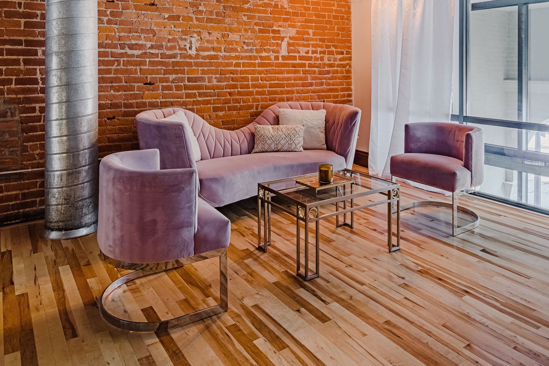 Modern lounge with purple chairs, glass tables, brick wall, and wood floor near large windows