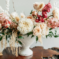 White vase with cream, pink, and dried floral arrangement on a wooden table