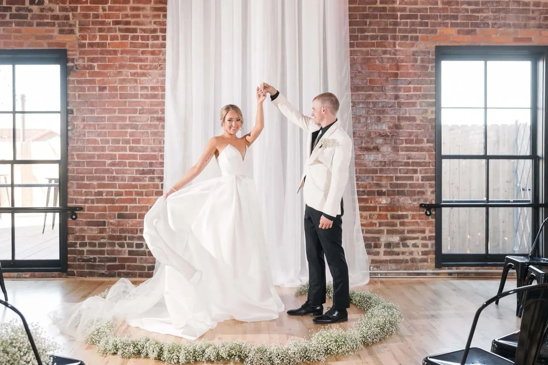 Bride and groom dancing on a small stage in a brick-walled loft venue