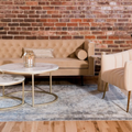 Cozy lounge with beige sofa, round marble tables, striped chairs, and a brick wall backdrop