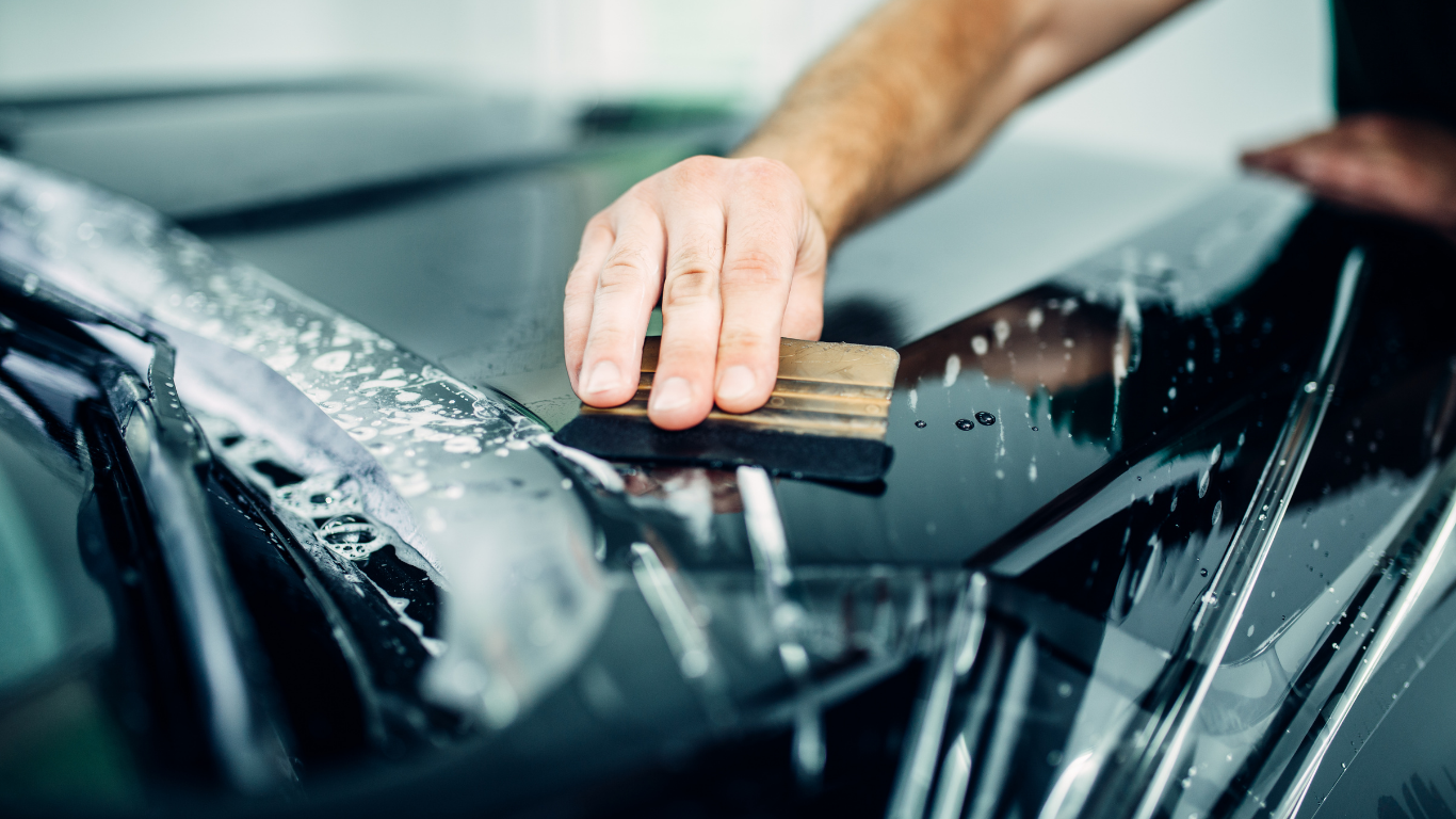 Person scrubbing a black car windshield with a sponge during a wash
