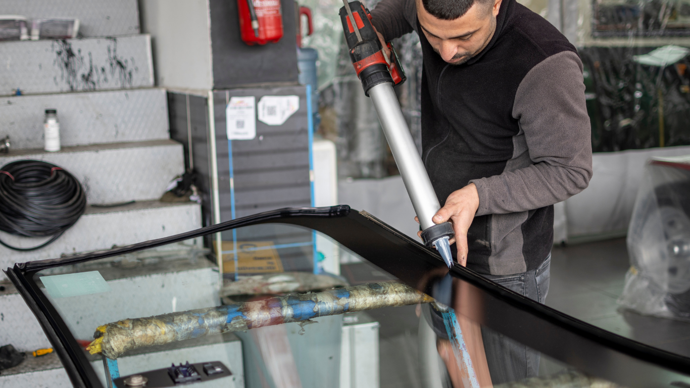 Man using a vacuum hose to clean a car windshield in a garage