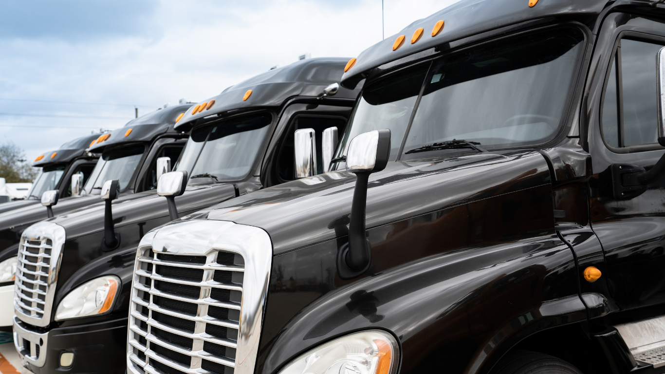 Row of black semi trucks parked side by side, front grilles facing forward