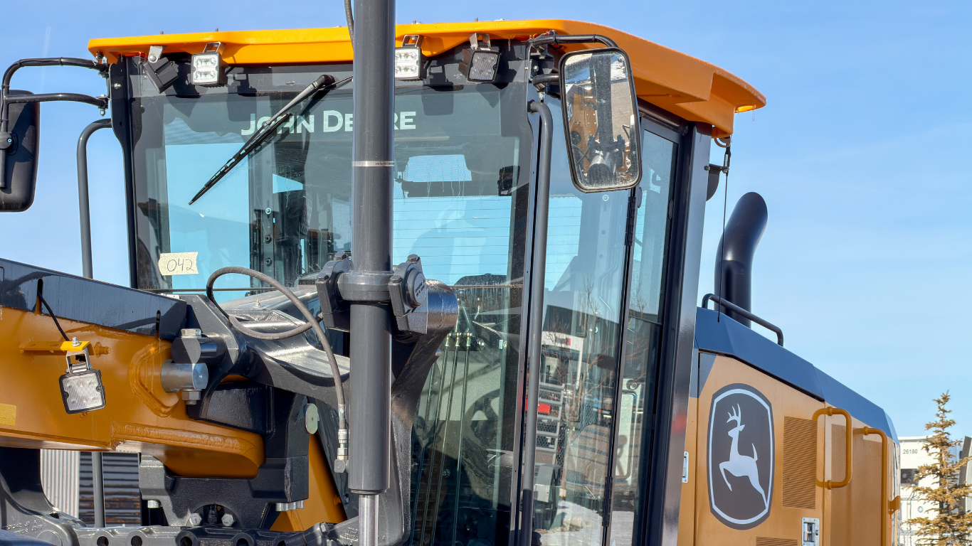 Orange construction loader cab with large windows and a black exhaust pipe against a blue sky