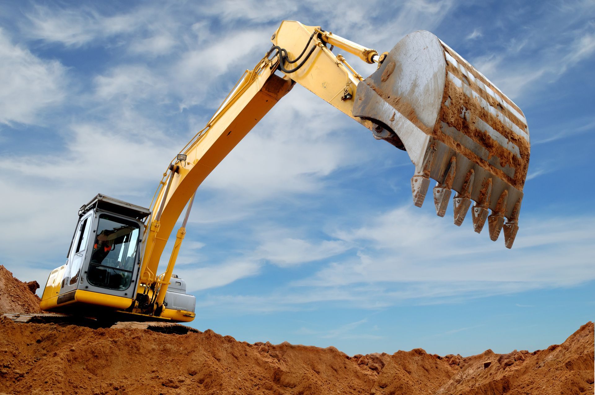 Yellow excavator with raised bucket working on a dirt mound construction site