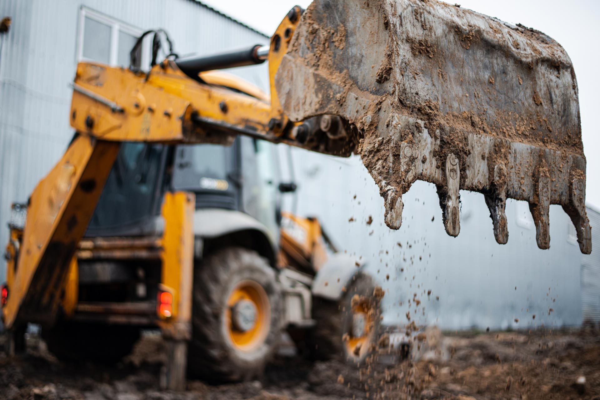 A yellow excavator bucket full of wet mud with soil dripping during site excavation work