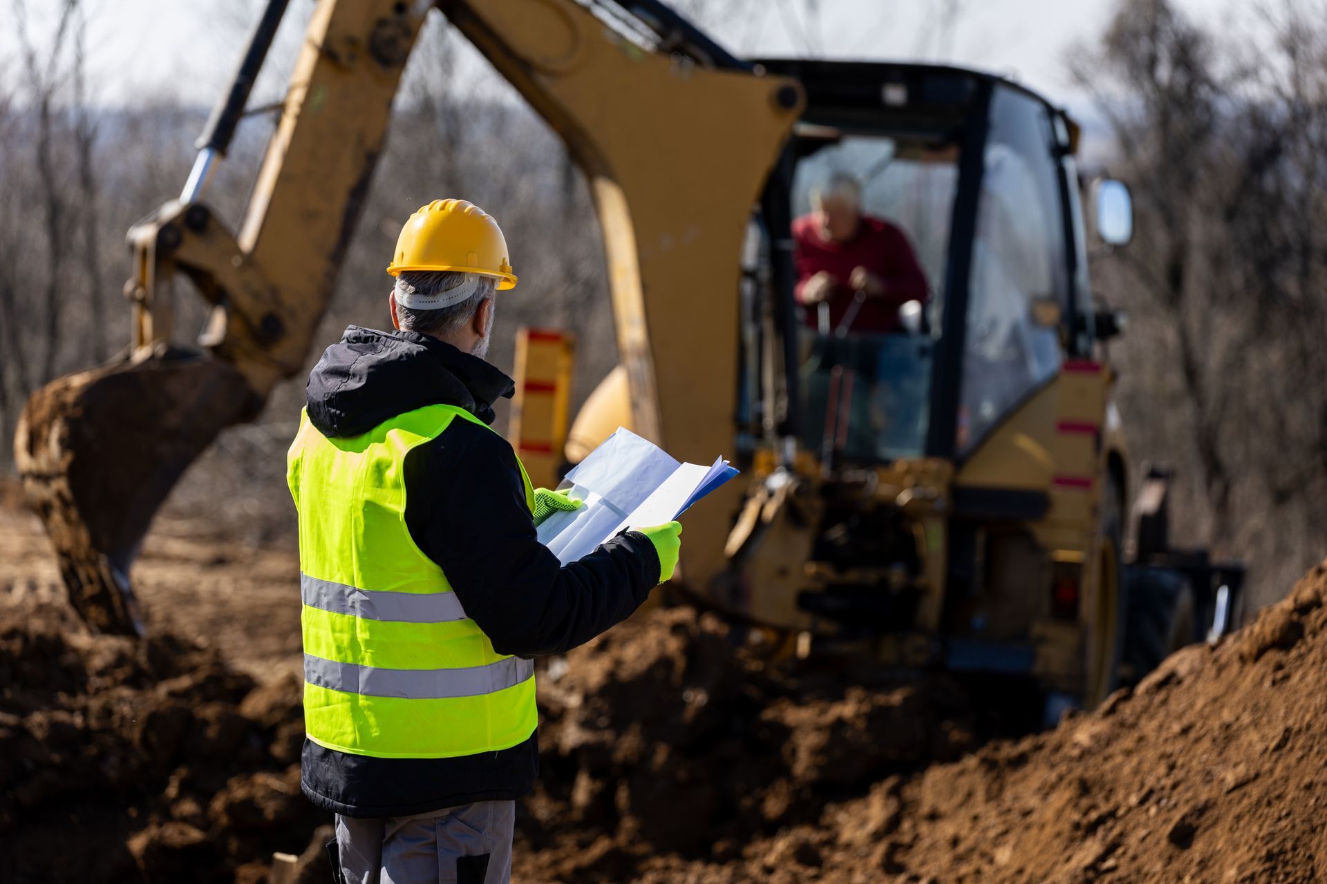 Site supervisor reviewing plans while an excavator works in the background