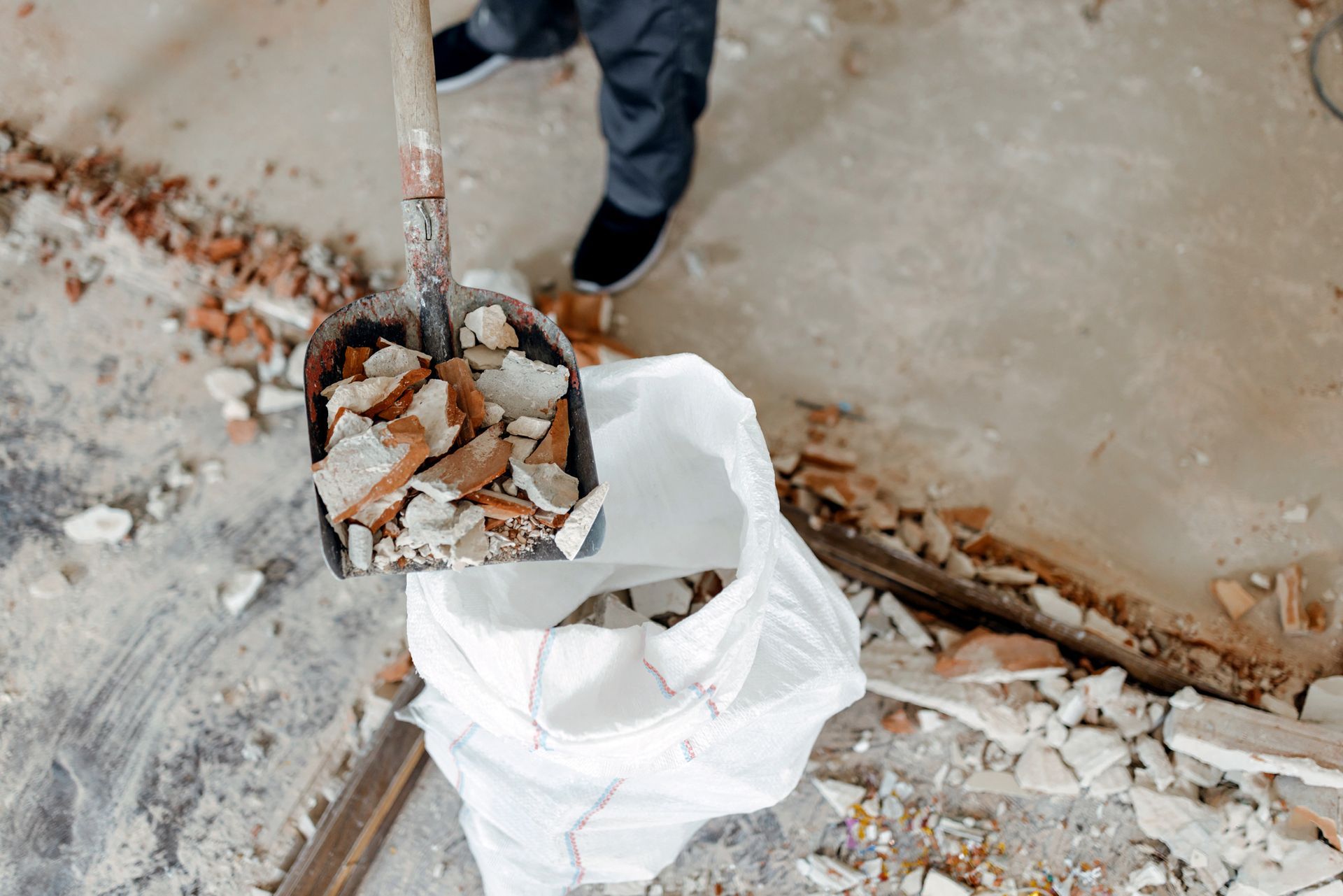 A person is holding a shovel filled with bricks and a bag of bricks.