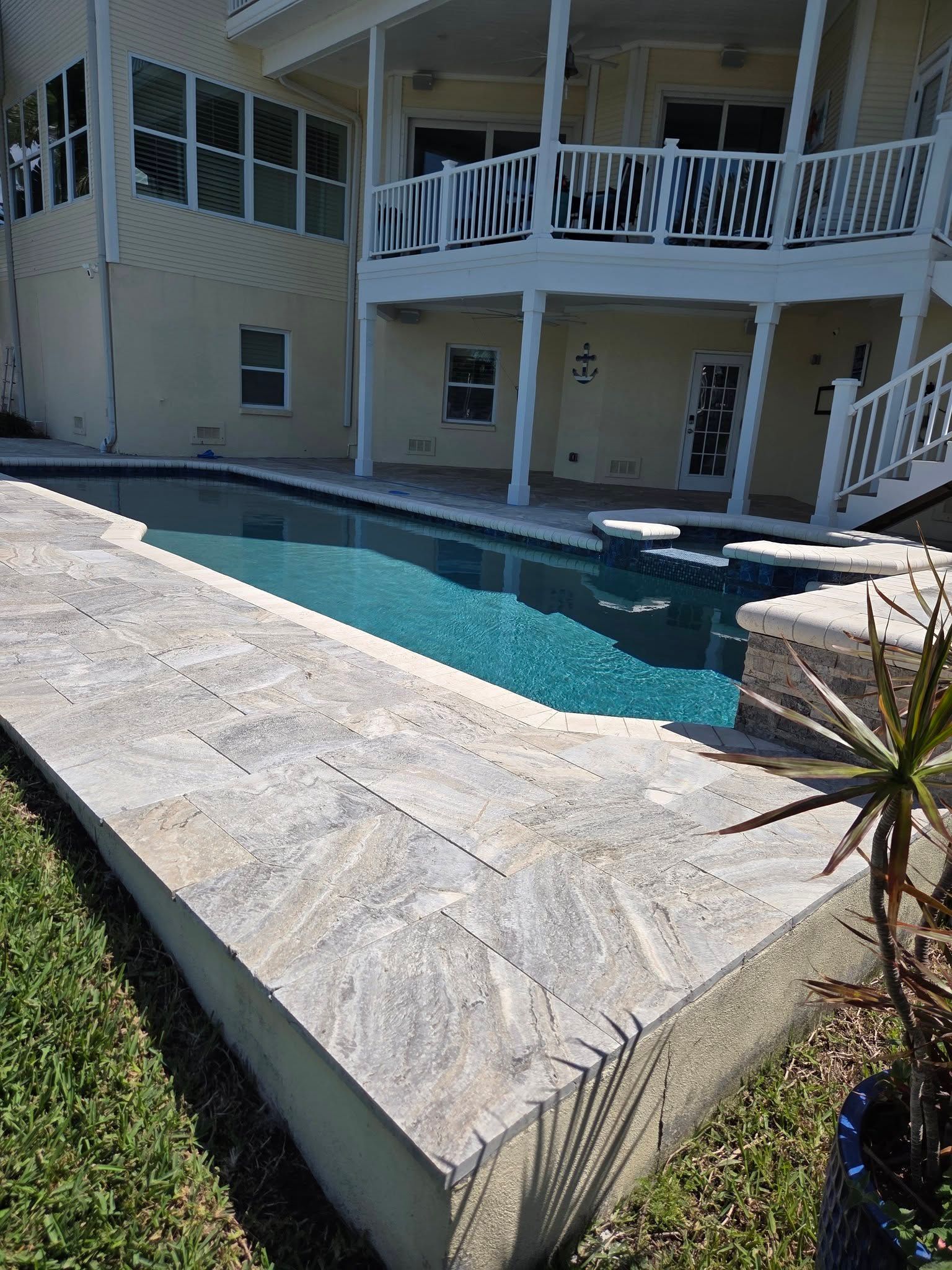 Backyard pool beside a white two-story house with covered balconies and stone coping