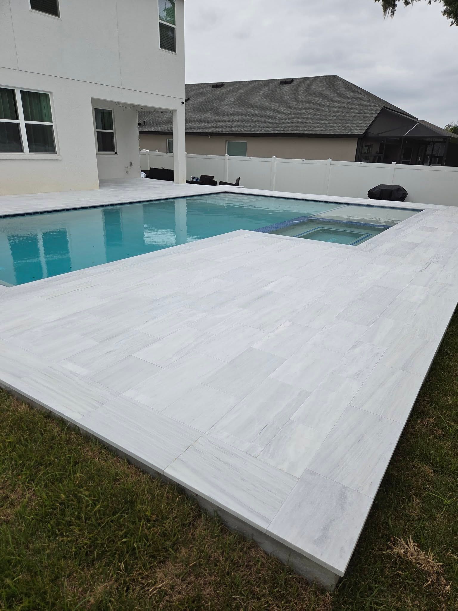 Backyard pool with white pool deck beside a modern house under a cloudy sky