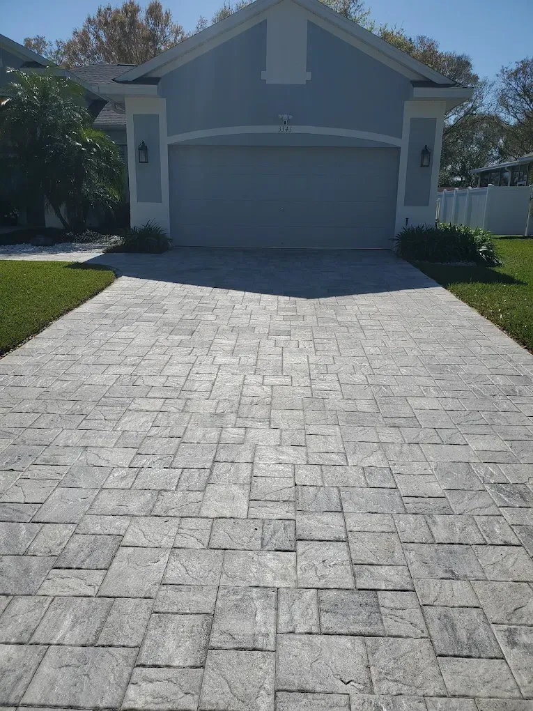 Front view of a house with a garage and a sunlit paver driveway.