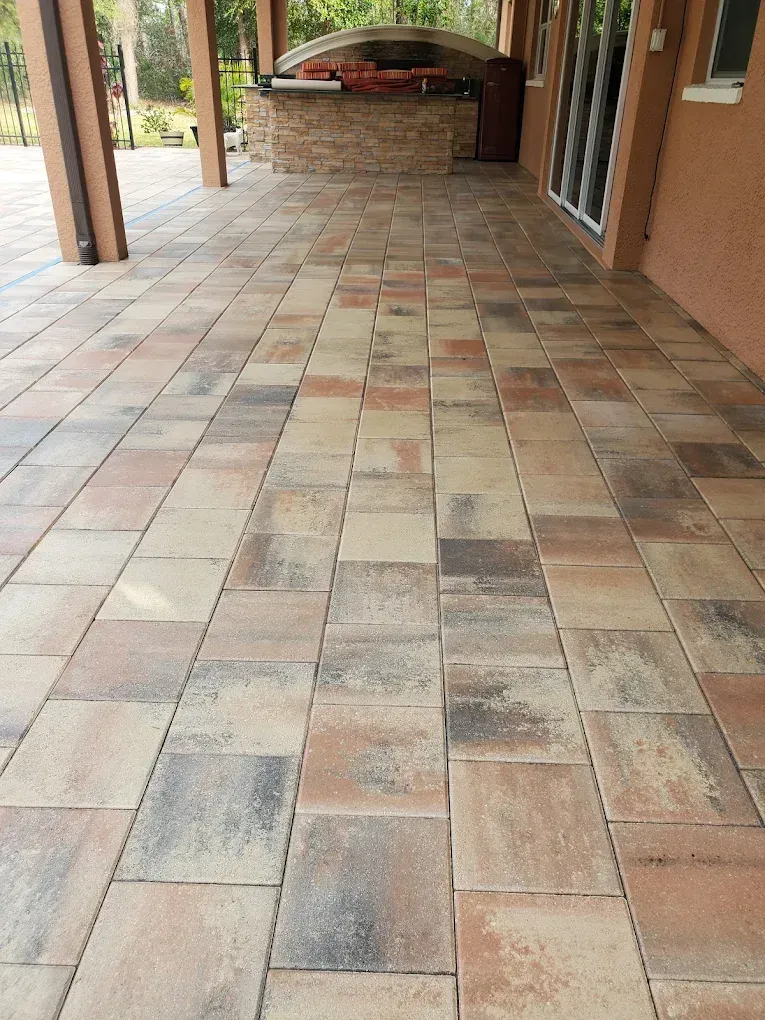 Covered outdoor walkway with tan and brown tiled floor and brick walls, leading to an arched opening.