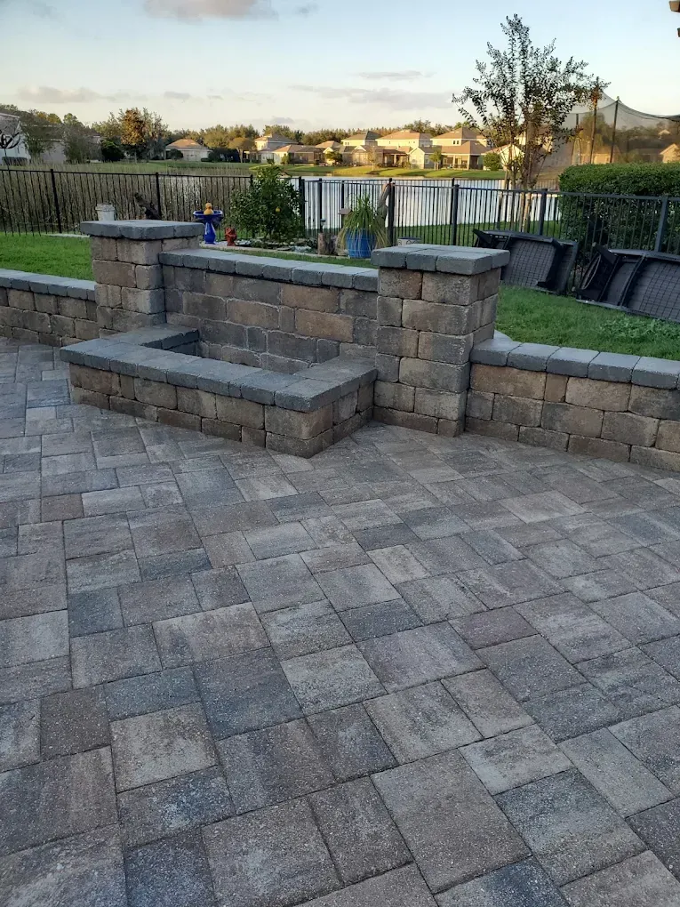 Stone patio with built-in bench and low wall overlooking a landscaped backyard and pond at sunset
