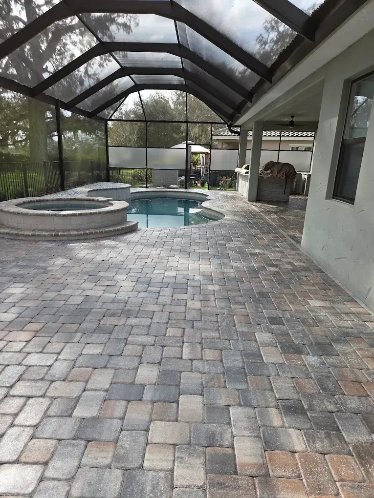 Screened patio with paver flooring, a spa, and a small pool under a glass roof.
