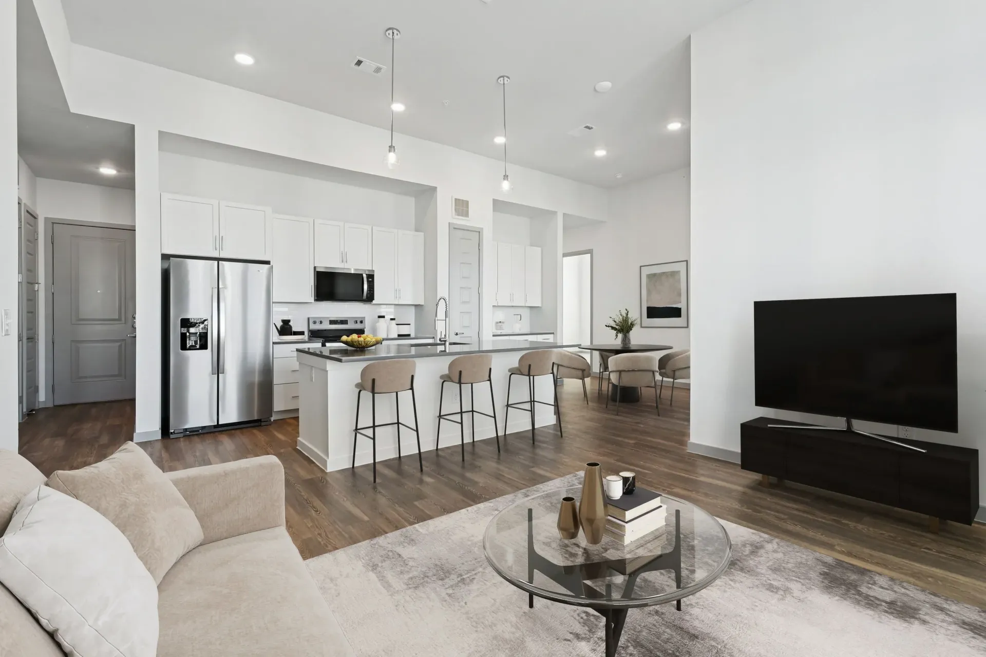 Open-concept kitchen and living area with white cabinets, stainless appliances, and a TV at Ennova Highlands apartments in Arlington, TX.