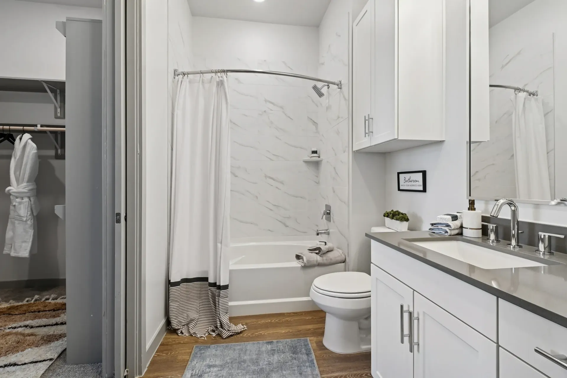 Modern white bathroom with marble-tile shower, shower curtain, toilet, and sink vanity at Ennova Highlands apartments in Arlington, TX.