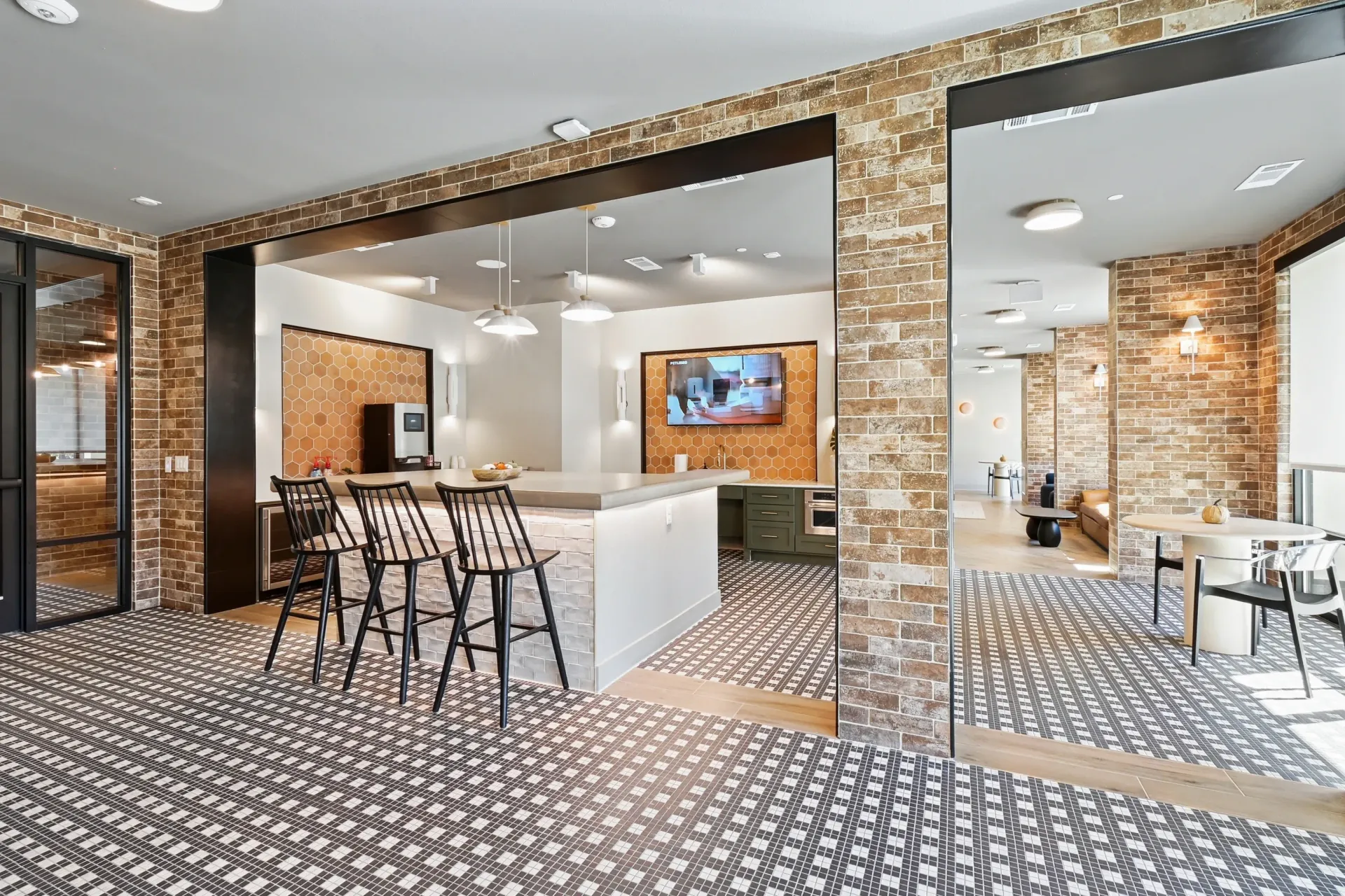Interior community lounge with brick walls, a kitchen island, and bar stools at Ennova Highlands apartments in Arlington, TX.