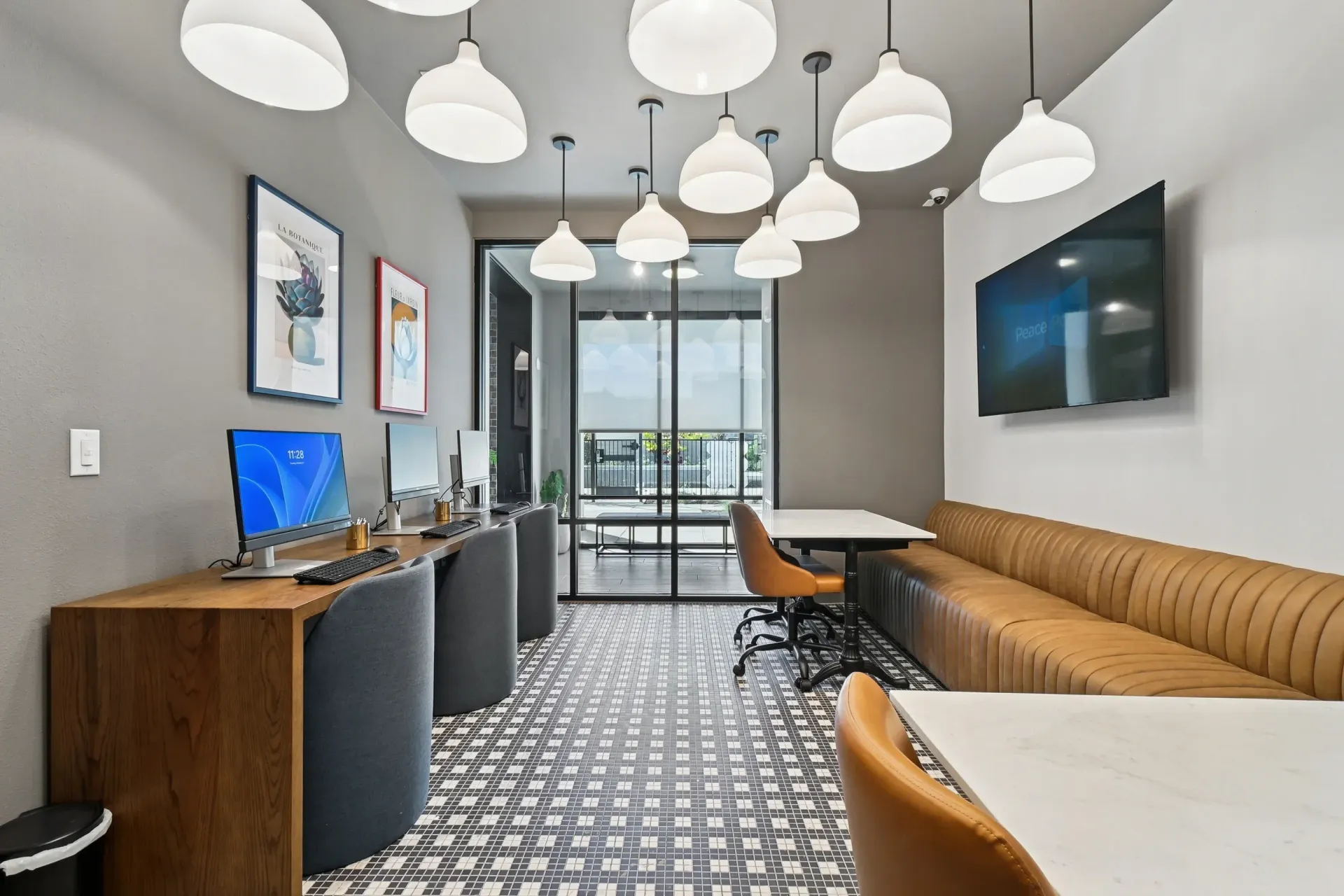 A modern business center or co-working lounge with computer stations, a long bench, and overhead globe lighting.