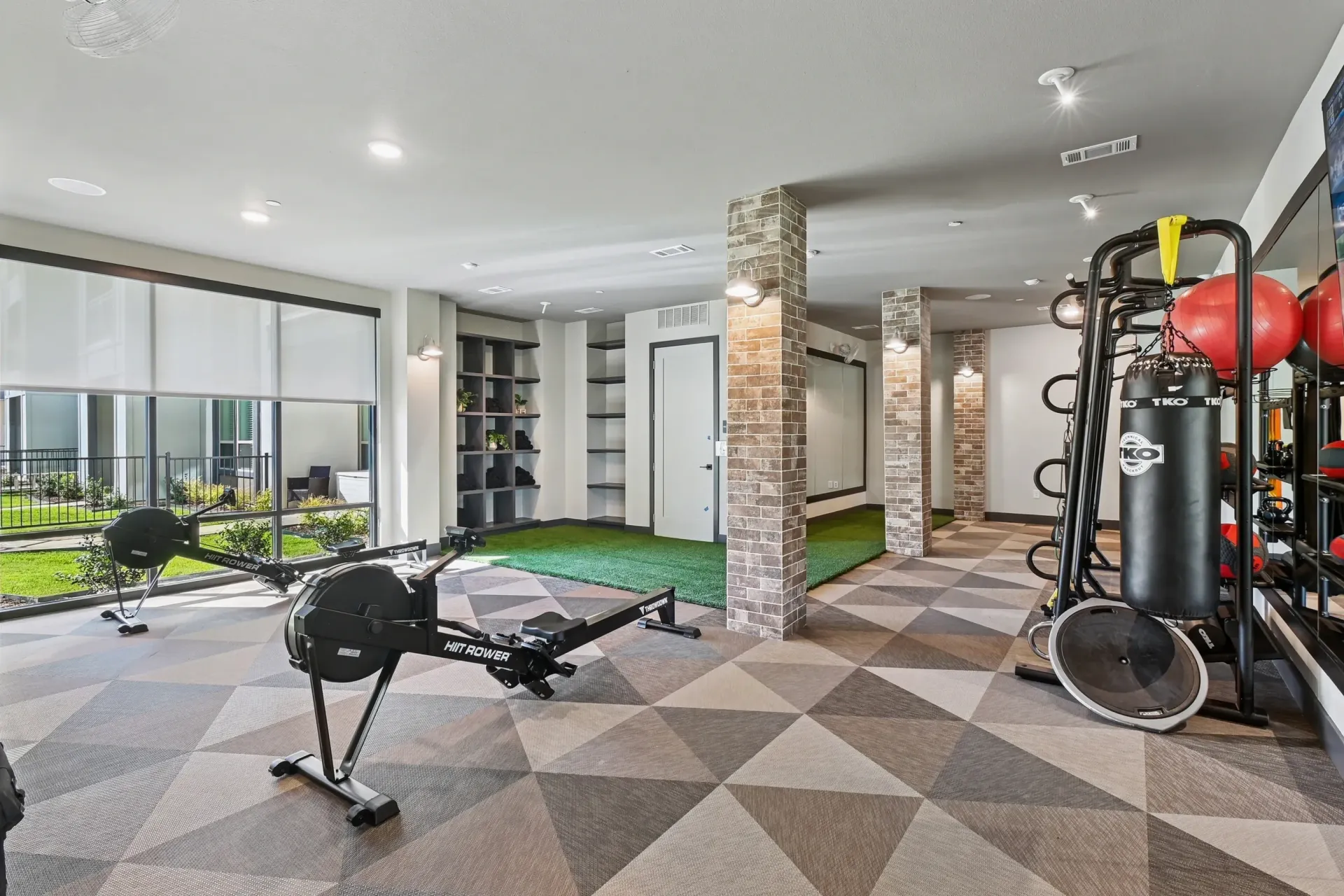 Interior of a community gym with cardio machines, weights, and turf at Ennova Highlands apartments in Arlington, TX.
