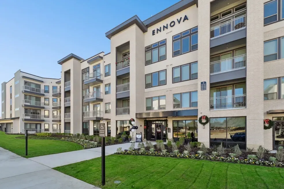 A modern, multi-story beige apartment complex named Ennova with balconies, glass windows, and landscaped front lawns.