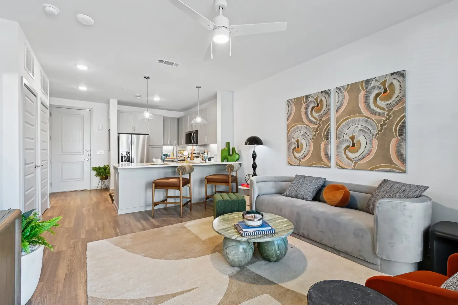Open-concept living room with grey sofa, kitchen island, pendant lights, and modern art at Ennova Highlands apartments in Arlington, TX.