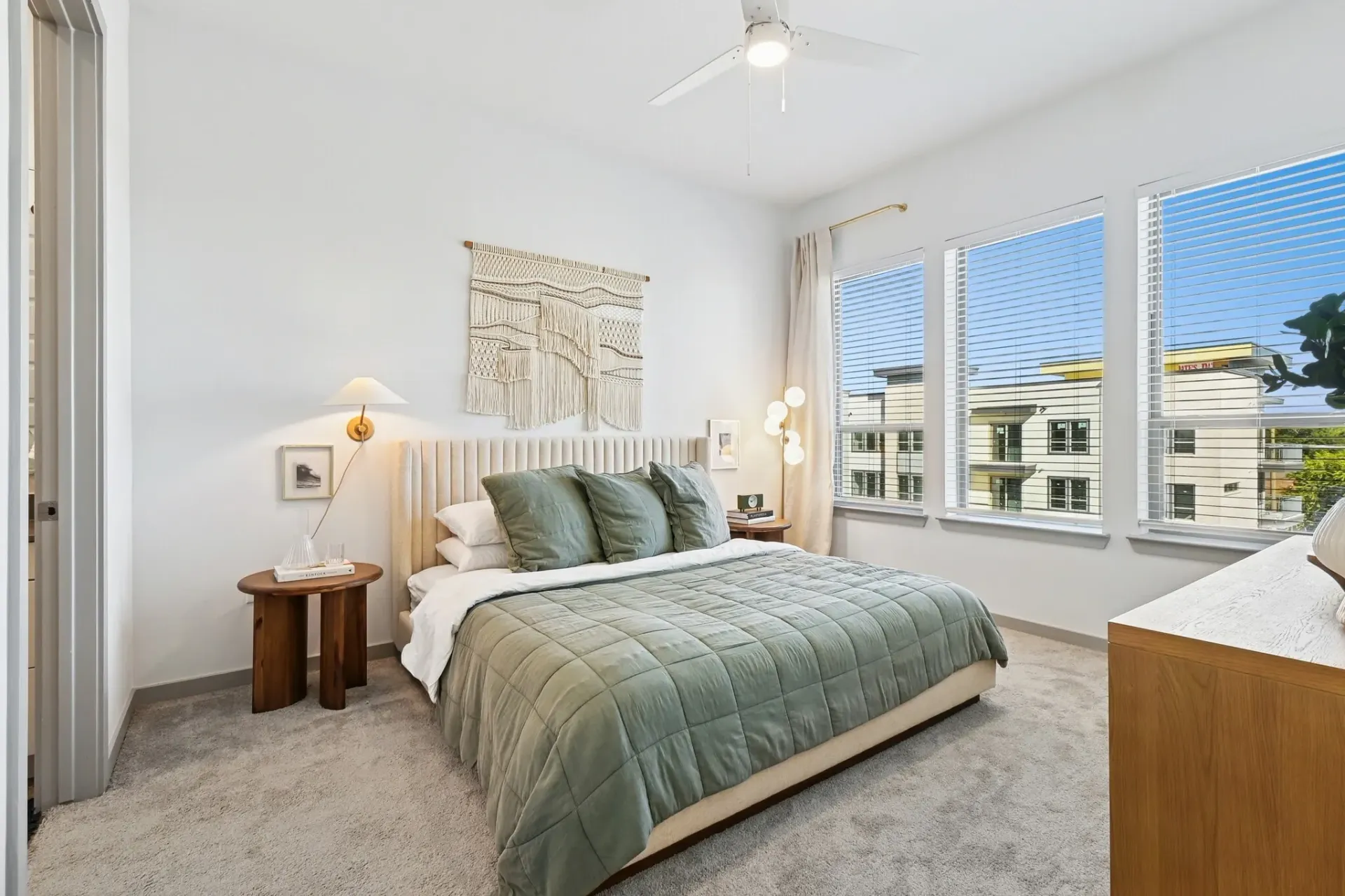 Bright bedroom in a modern apartment with a plush bed, sage bedding, and large windows at Ennova Highlands apartments in Arlington, TX.