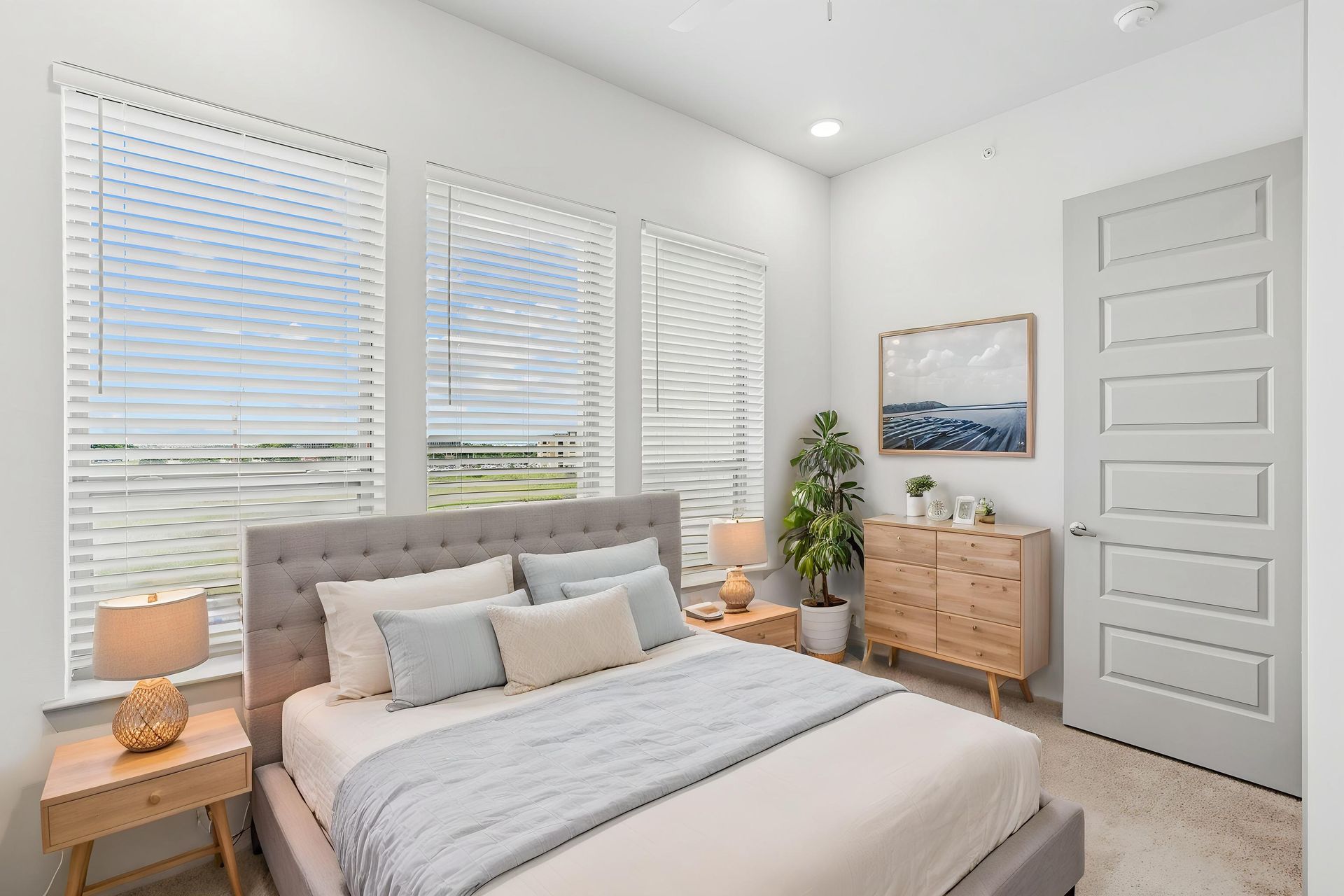Bright bedroom with gray bed, white shutters, wood nightstands, dresser, and coastal wall art