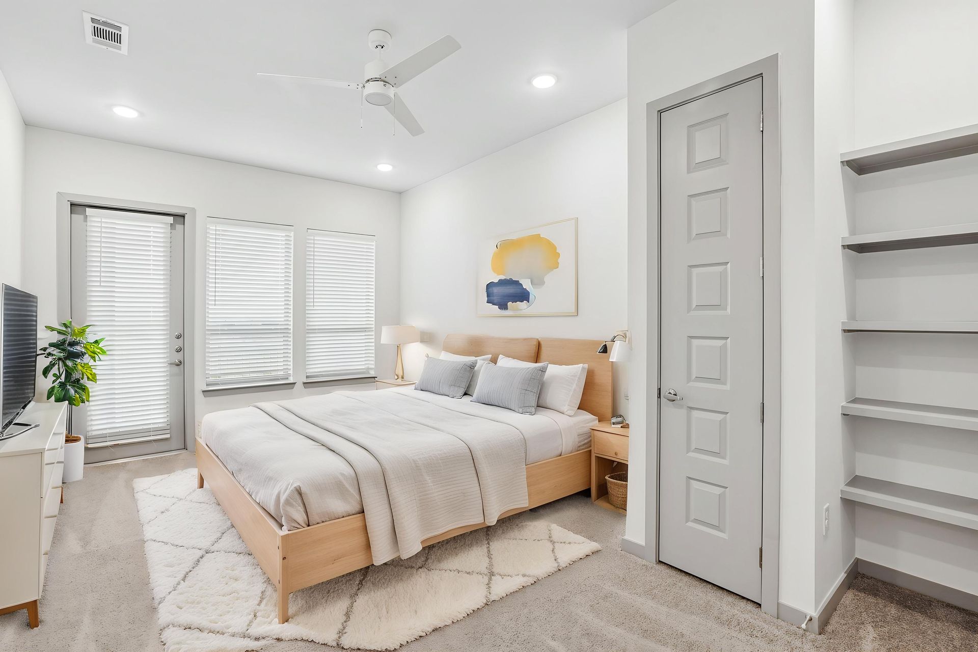 Bright modern bedroom with a white bed, ceiling fan, large windows, and built-in shelves