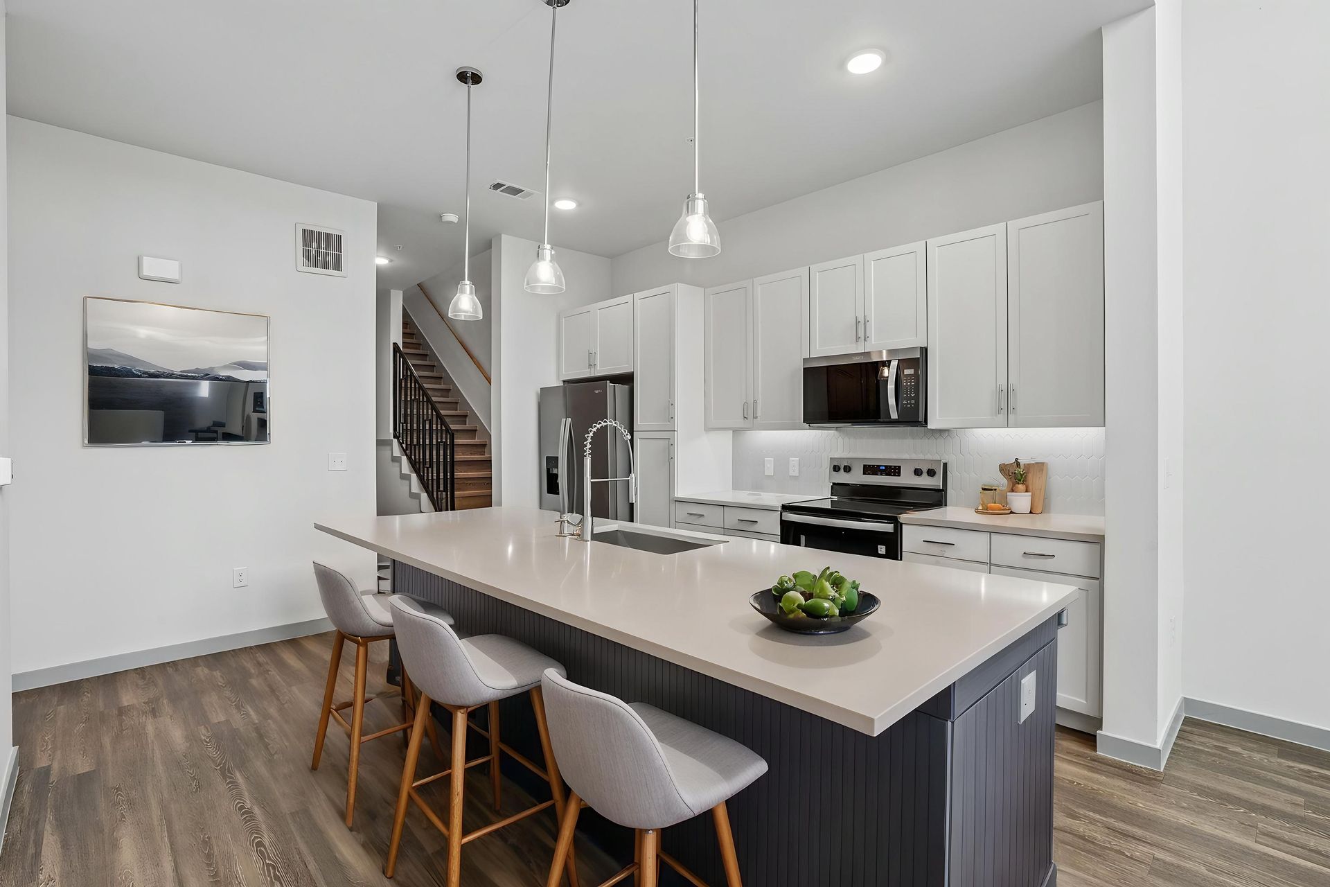 Modern white kitchen with island, gray barstools, pendant lights, and stainless steel appliances