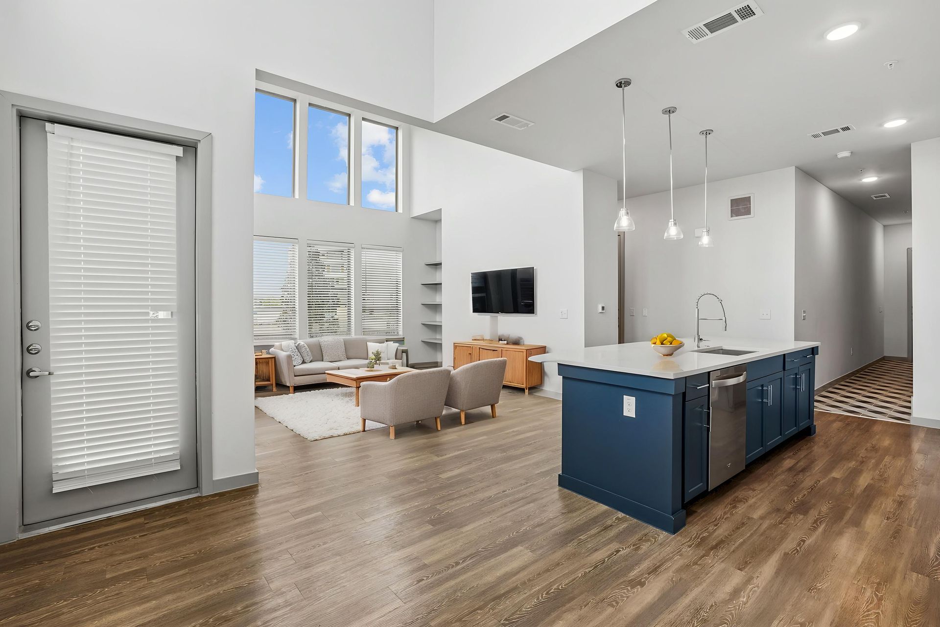 Bright modern living room with blue kitchen island, wood floors, and large windows