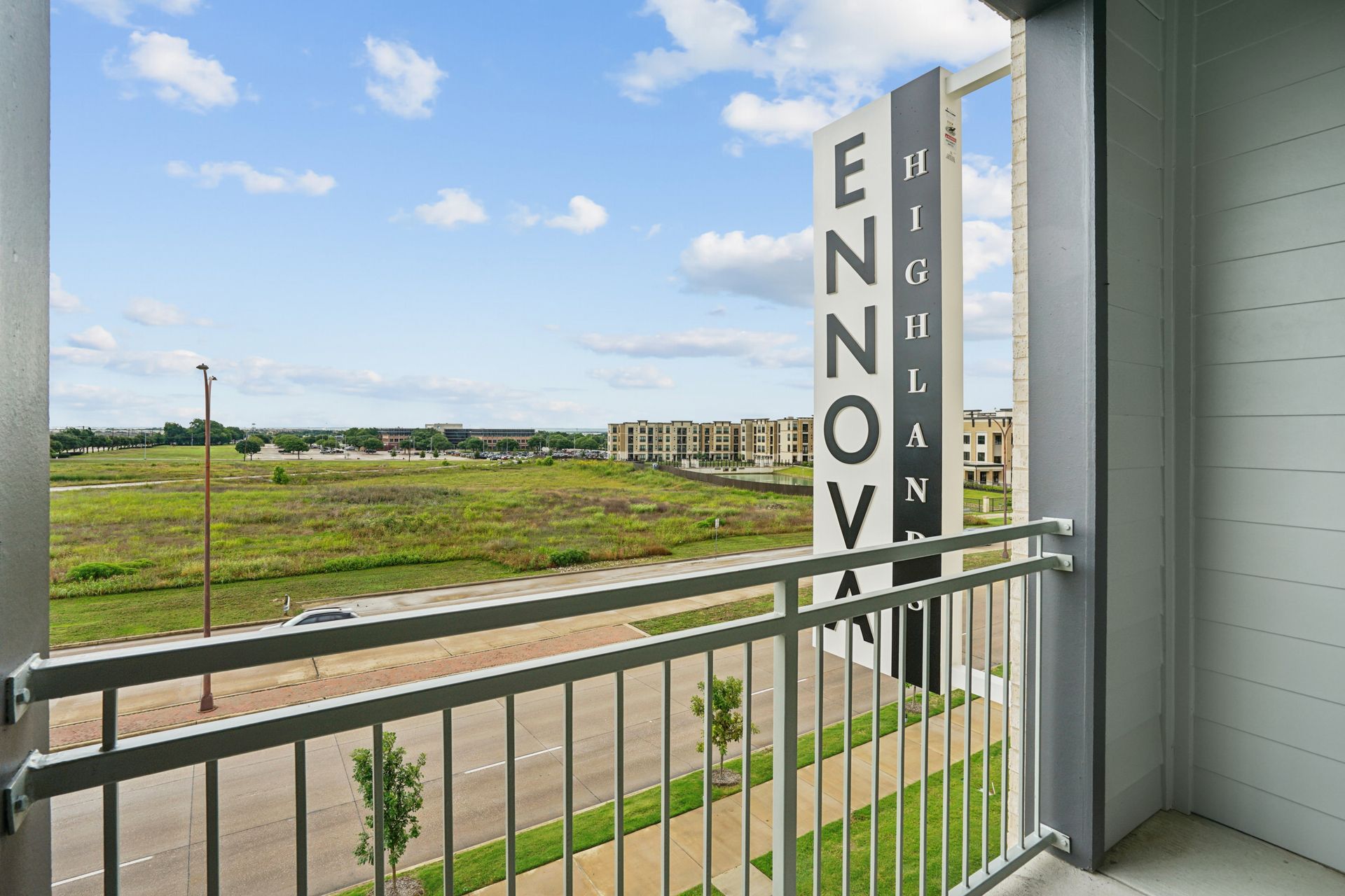 Balcony view of open field and buildings, with a vertical ENOVA sign on a nearby tower.