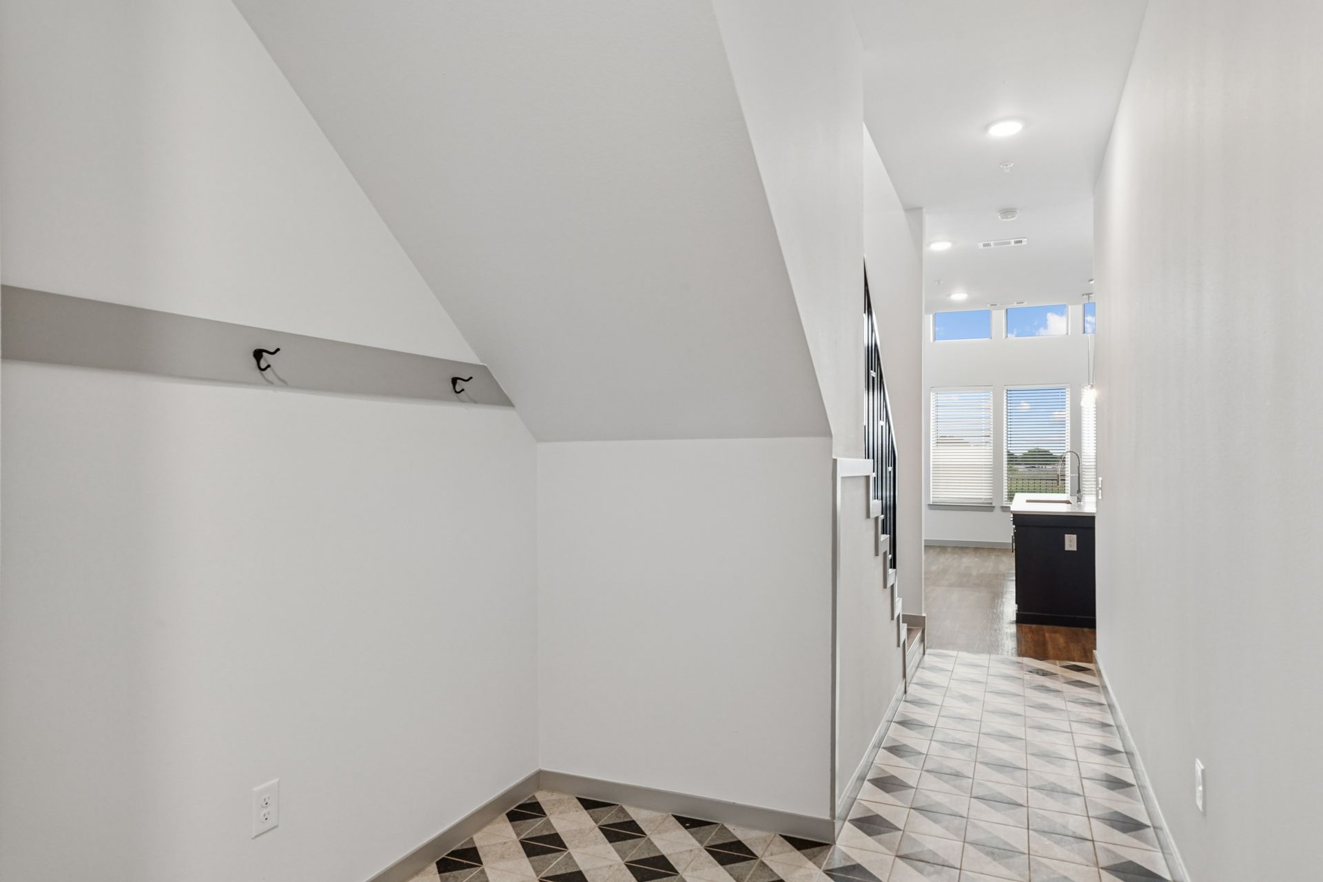 Bright white hallway with sloped ceiling, patterned tile floor, and a windowed door at the end.
