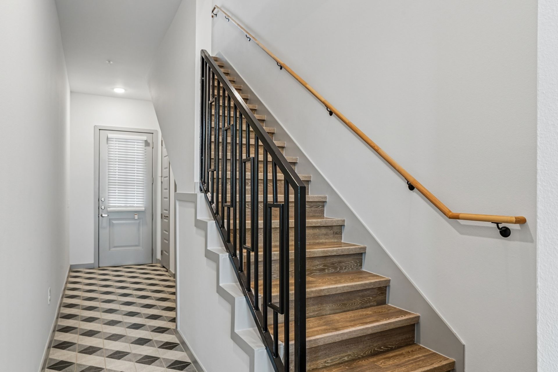 Hallway with patterned tile floor and staircase with black railing and wooden handrail