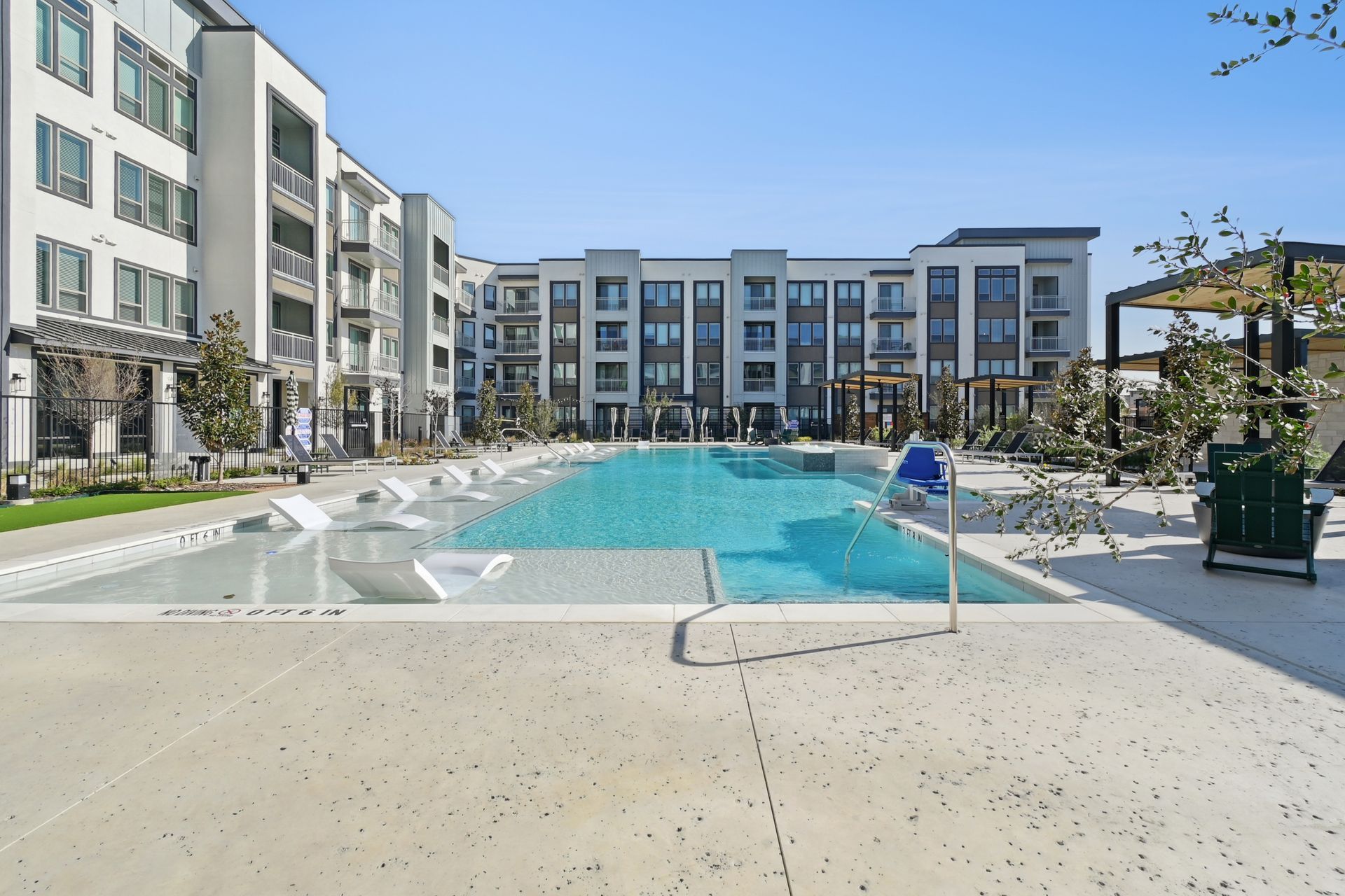 Modern apartment complex courtyard with a swimming pool, lounge chairs, and landscaped seating areas