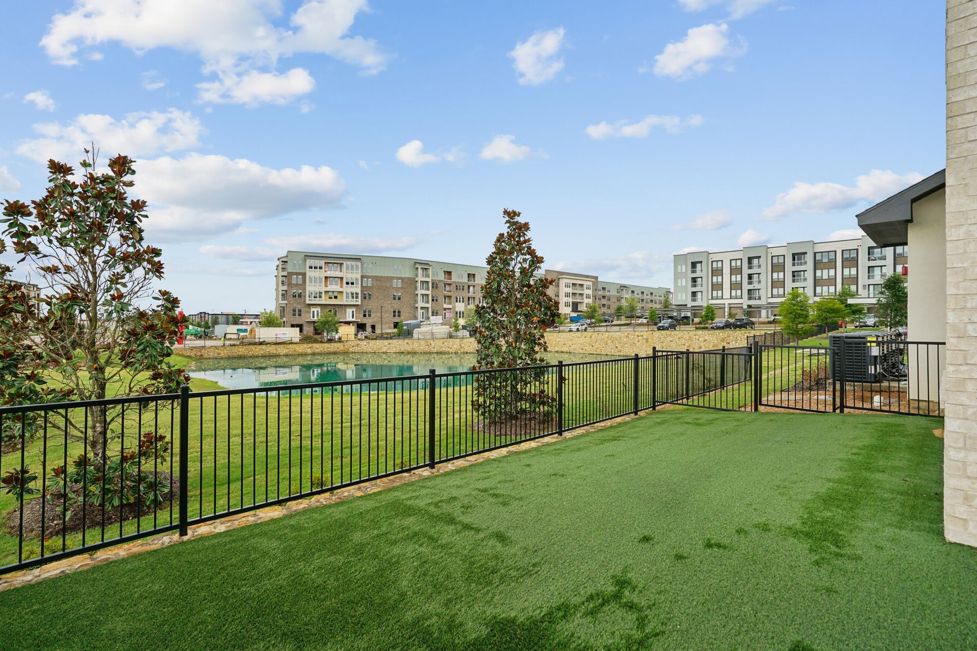 Grassy patio overlooking a pond and apartment buildings under a partly cloudy sky