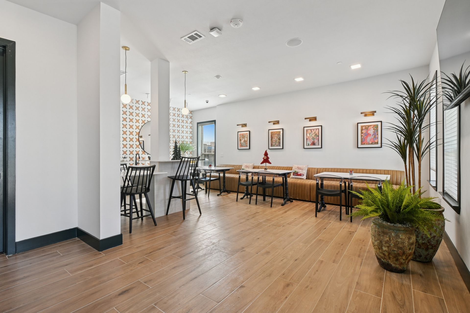 Bright modern lounge with wooden floors, benches, bar stools, framed art, and potted plants.